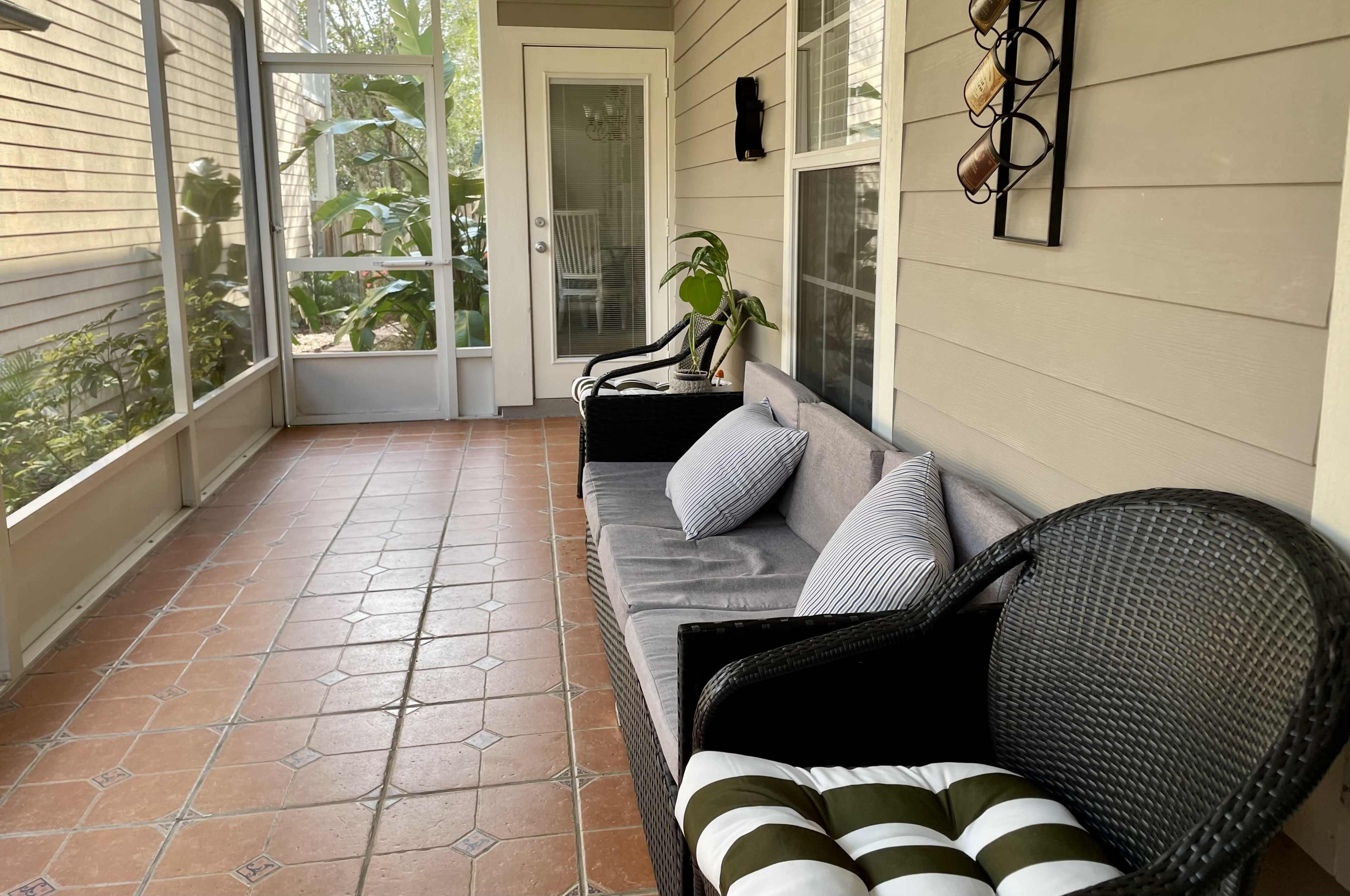 The image shows a screened porch with two wicker sofas adorned with cushions, and a tiled floor.