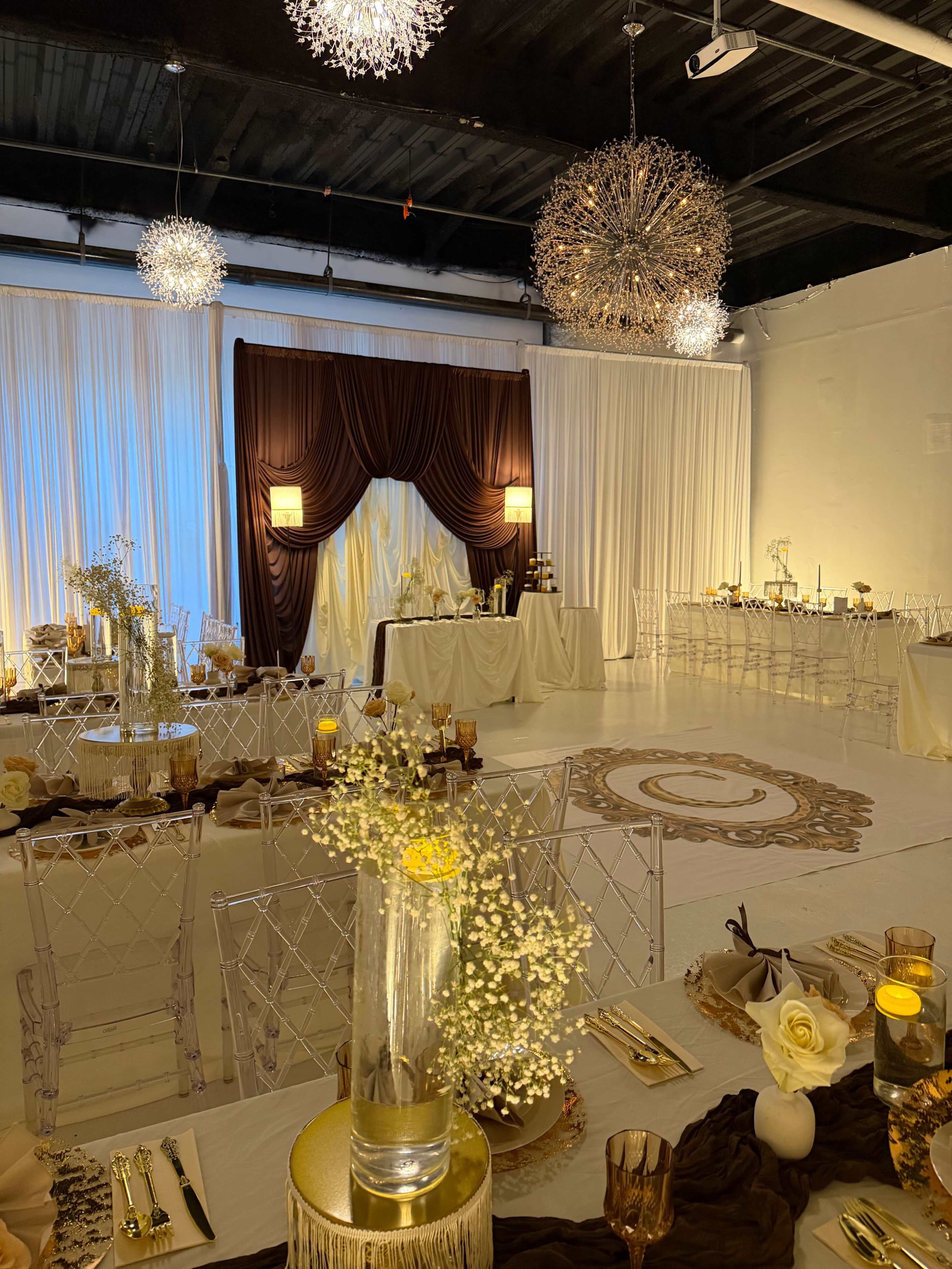 The image shows a beautifully decorated event space with elegant tables set and a backdrop featuring draped fabric and decorative lighting.