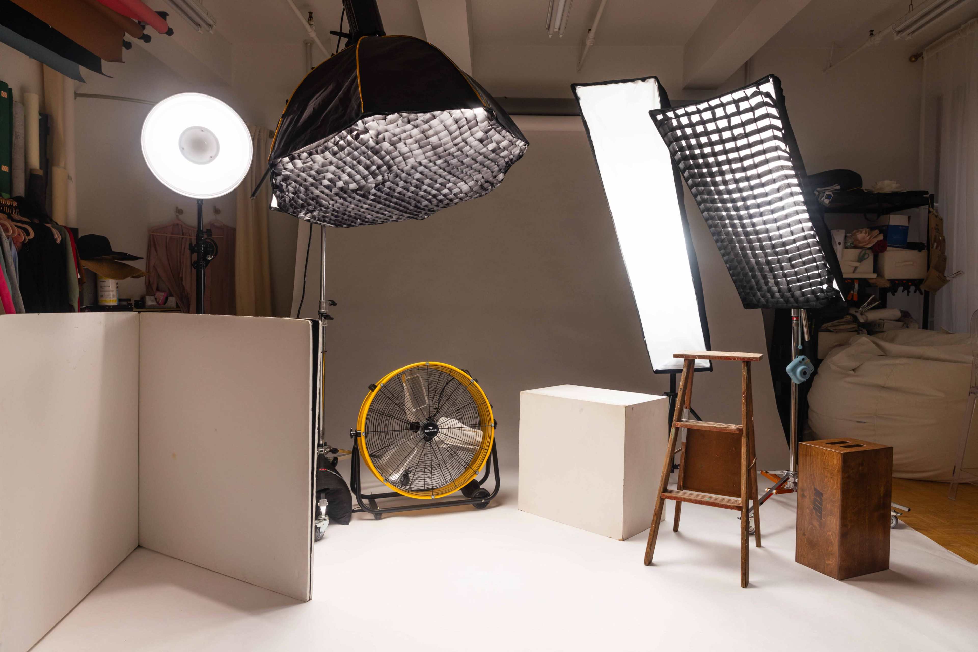 A photography studio setup features multiple lighting equipment, a wooden ladder, and various backdrops.