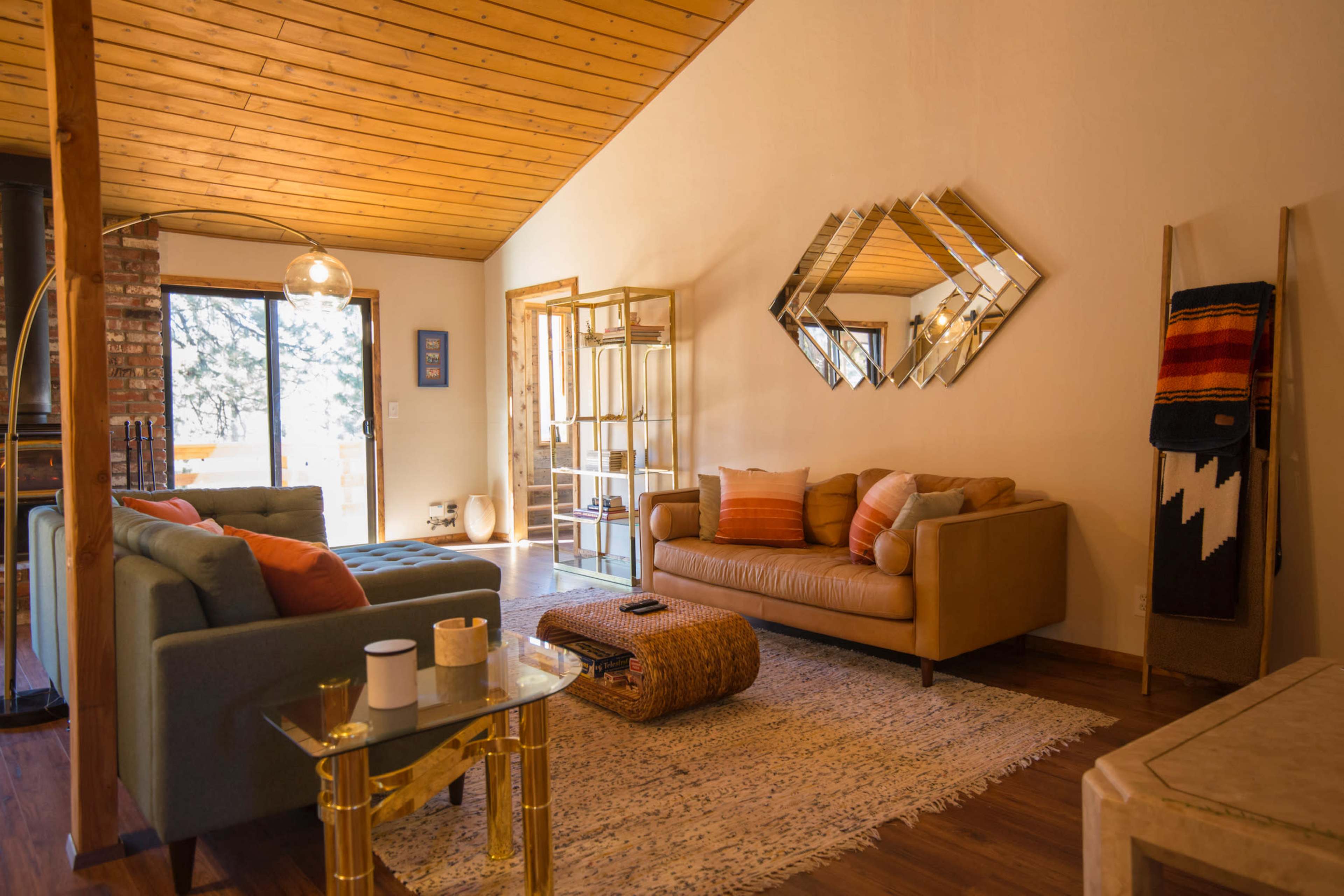 A cozy living room with two sofas, a coffee table, and a decorative mirror on the wall, surrounded by large windows that let in natural light.
