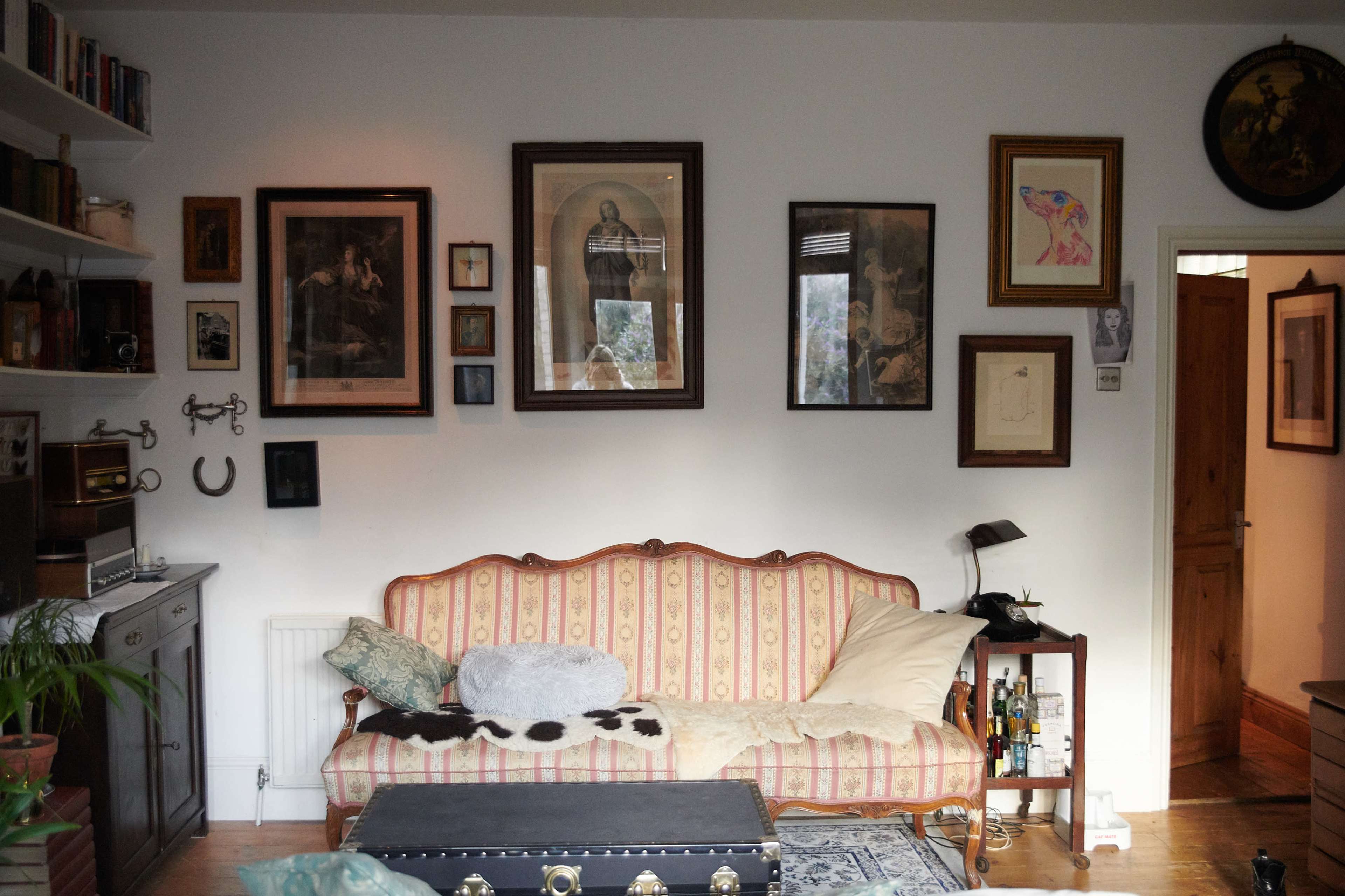 A living room wall with various framed artworks, a sofa with cushions, and a doorway leading to another room.