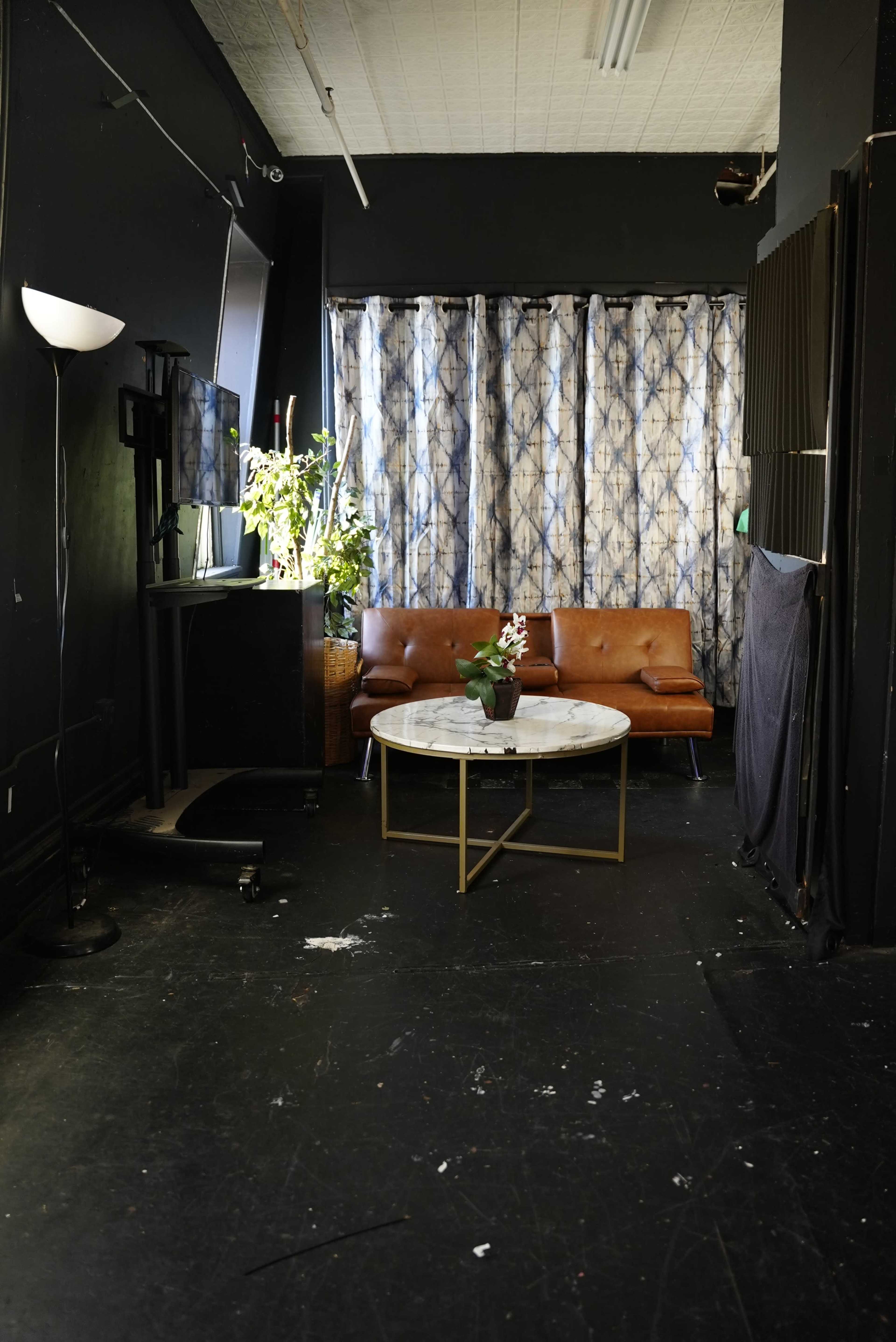 The image shows a dimly lit room with a brown leather couch, a round marble table, and patterned curtains in the background.