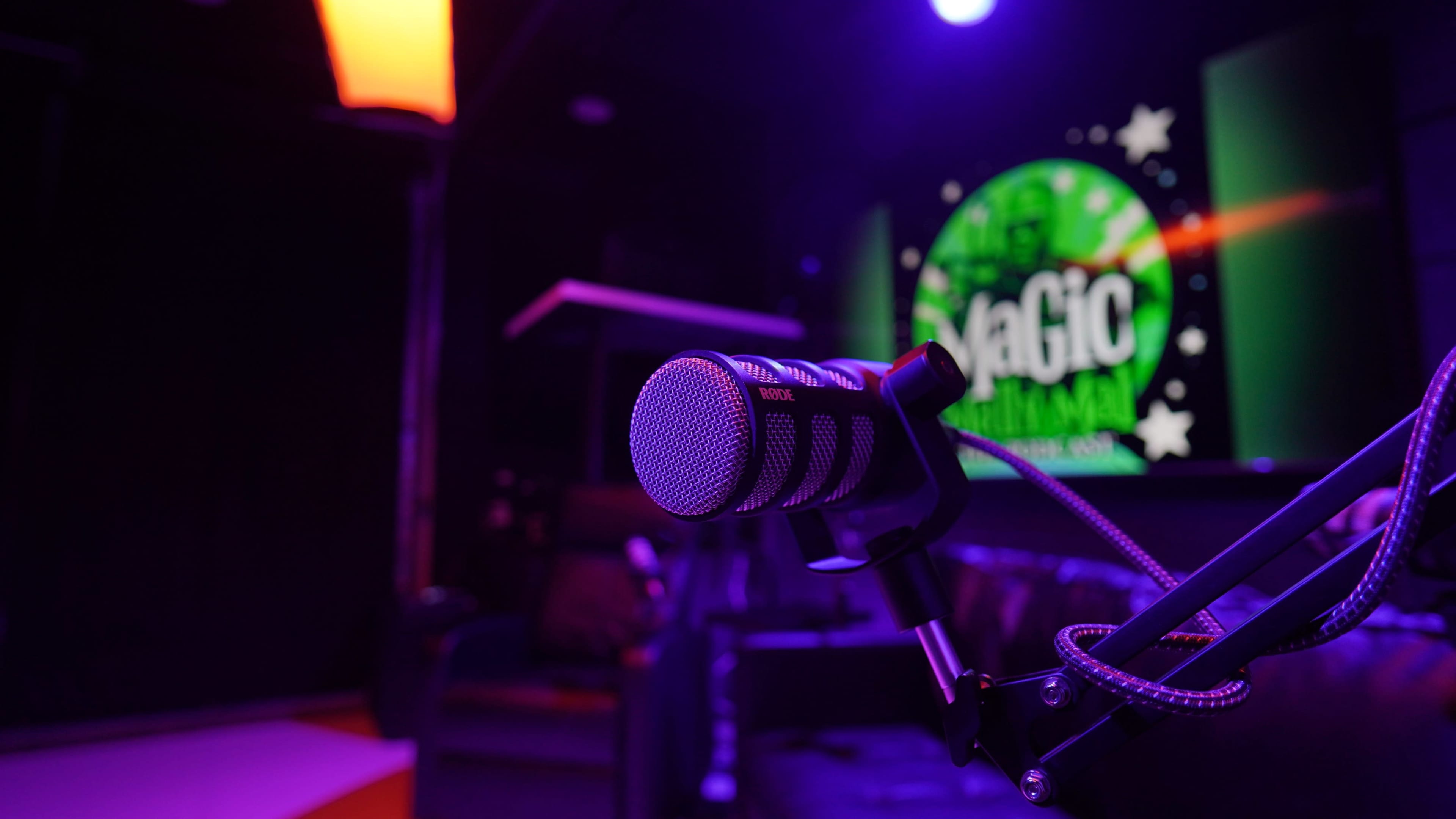 A microphone is positioned on a stand in a dimly lit room with colorful lighting and a promotional backdrop featuring "Magic."