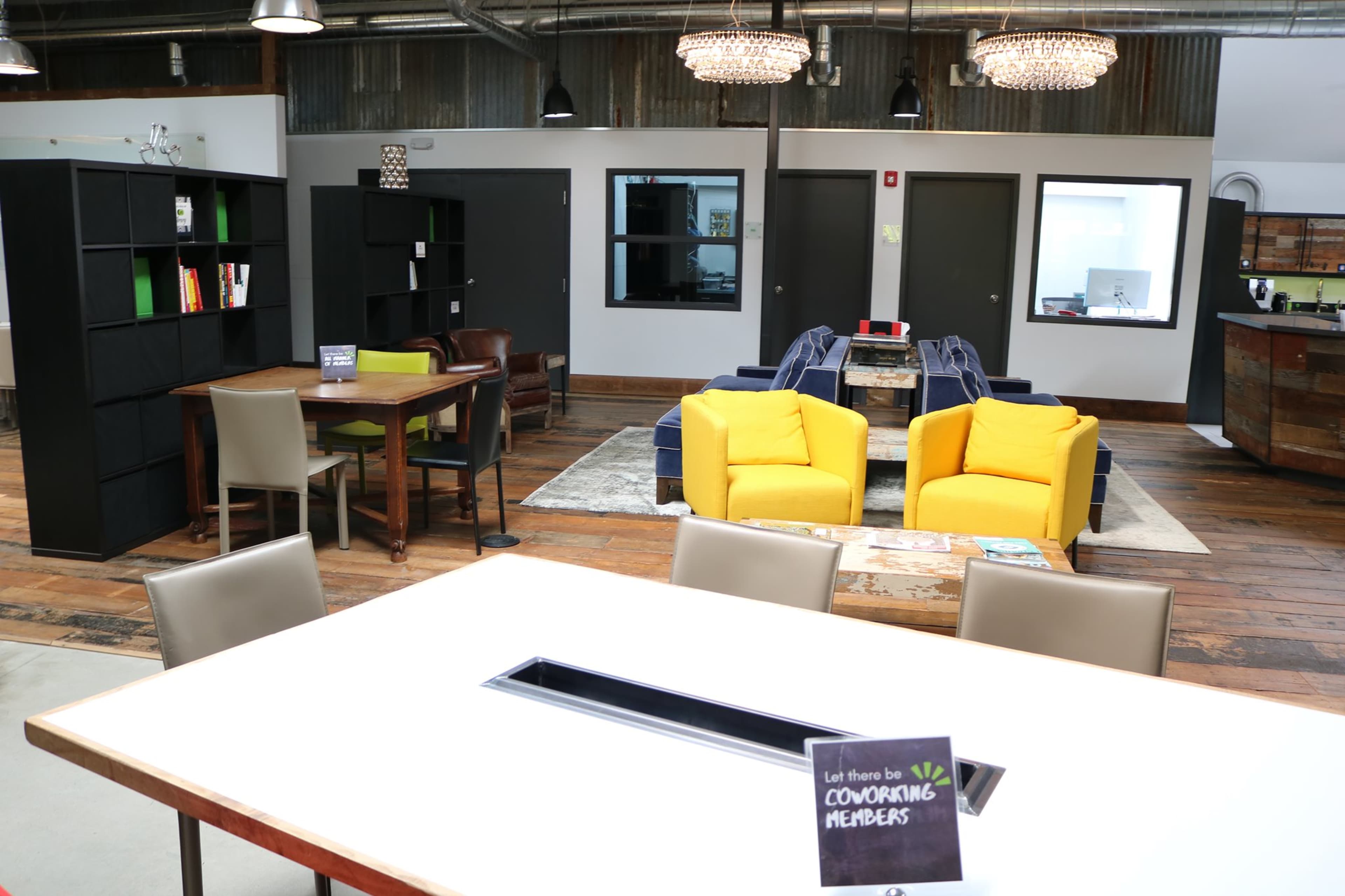 A modern coworking space featuring yellow lounge chairs, wooden flooring, and shelves filled with books.