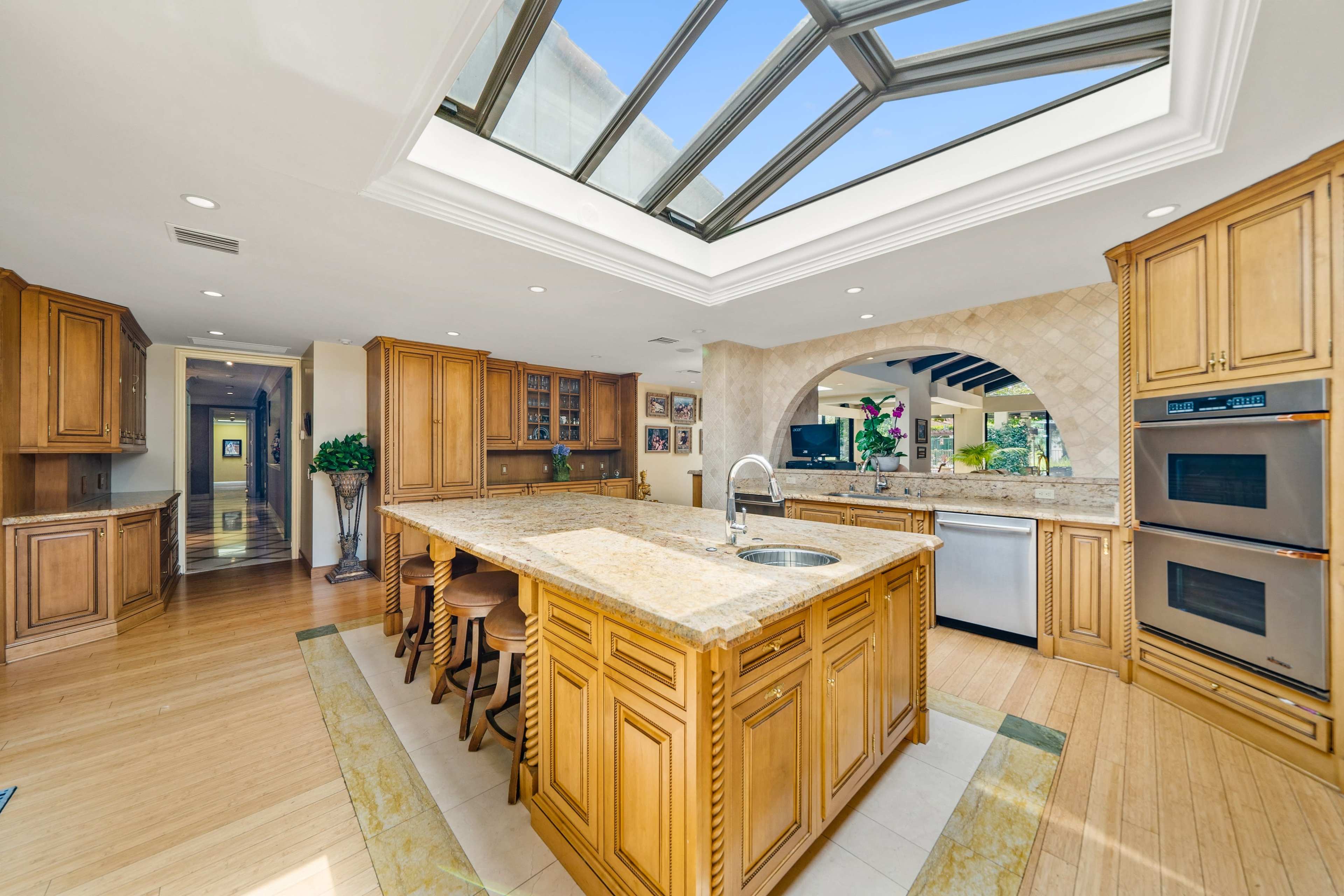 The kitchen features light wooden cabinetry, a large island with a granite countertop, and a skylight that illuminates the space.