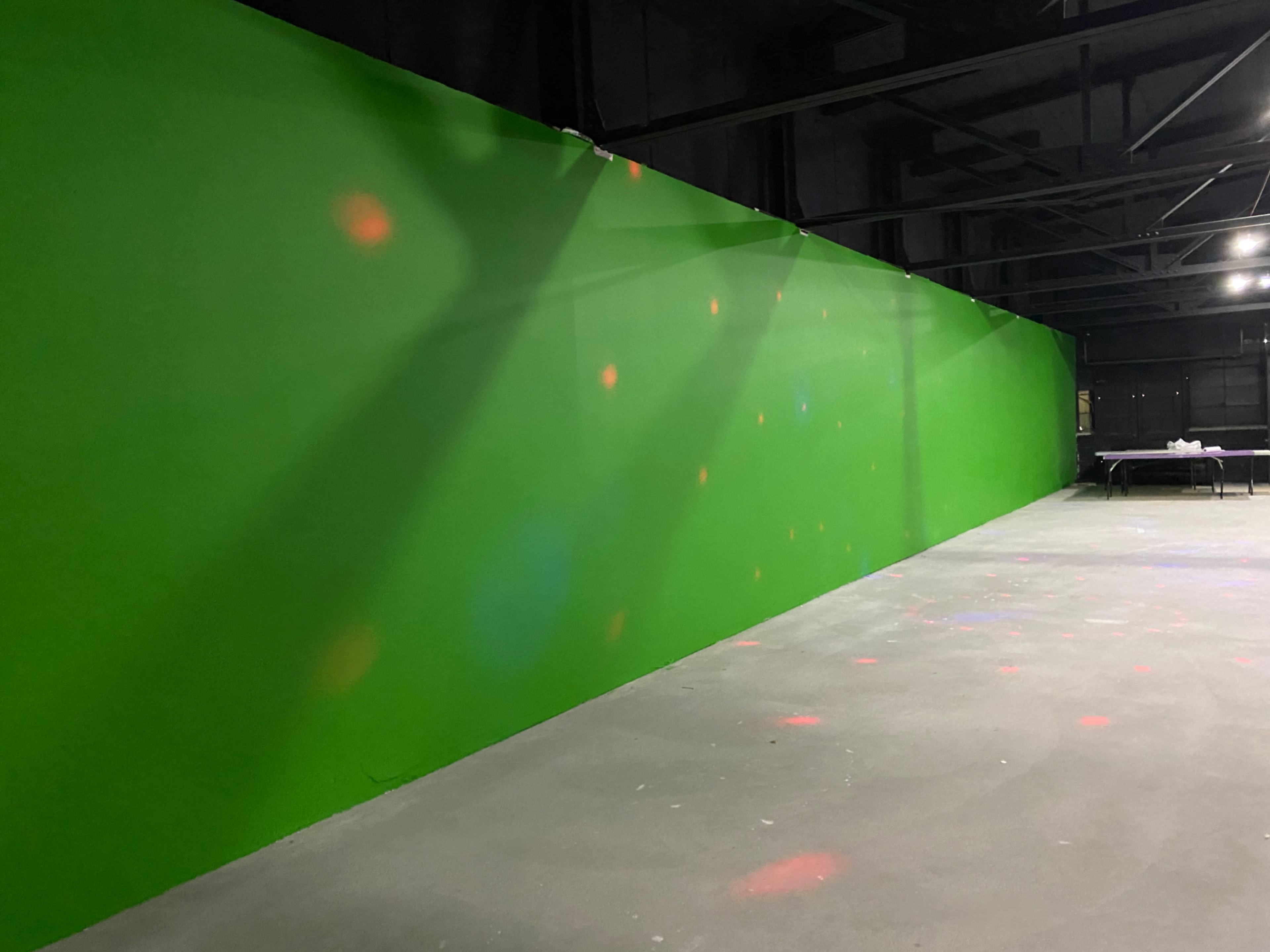 The image shows a large green wall in an industrial space with scattered colored lights on the floor.