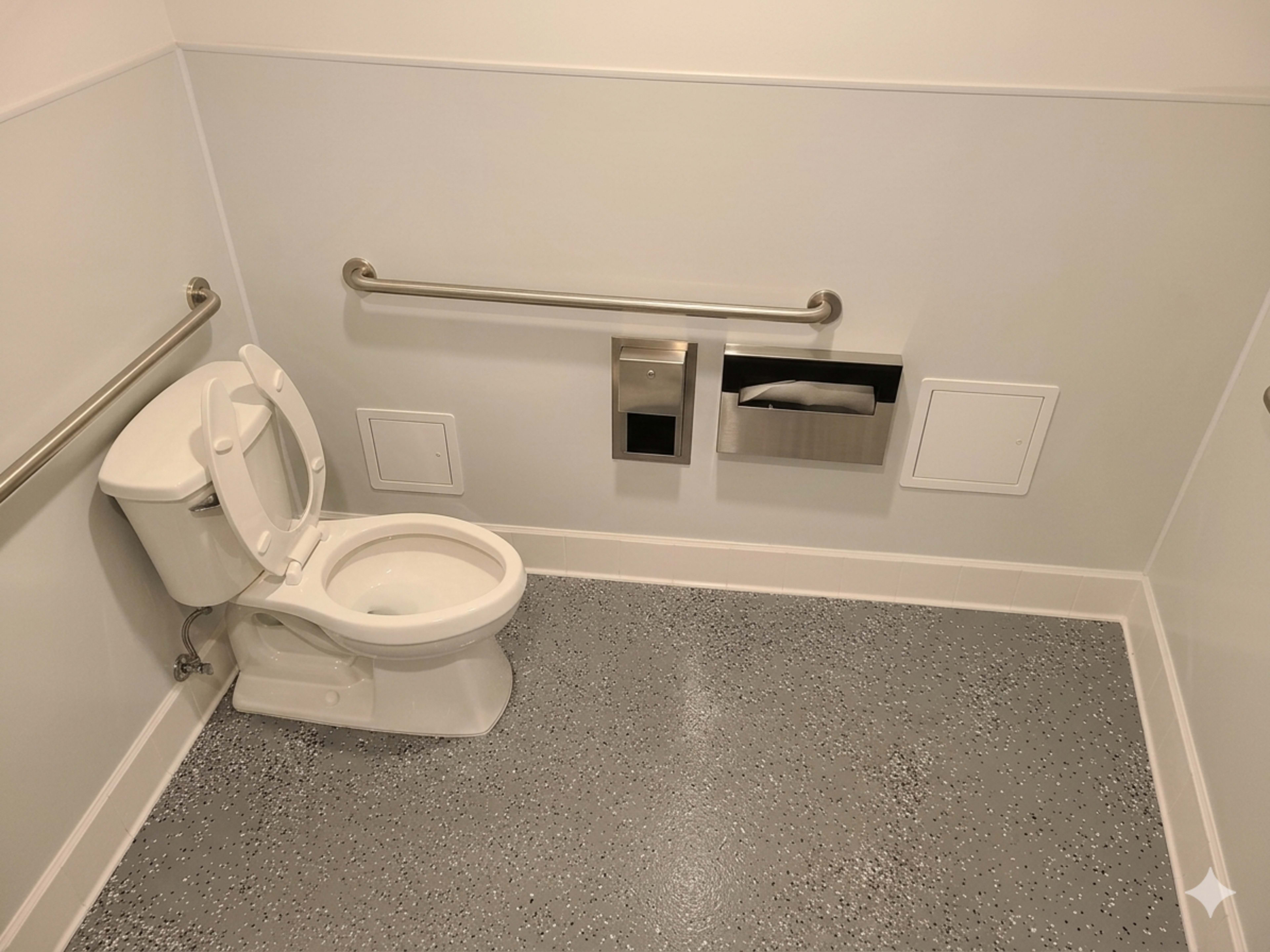 The image shows a clean restroom stall featuring a toilet, grab bars on the walls, and tissue and waste disposal holders.