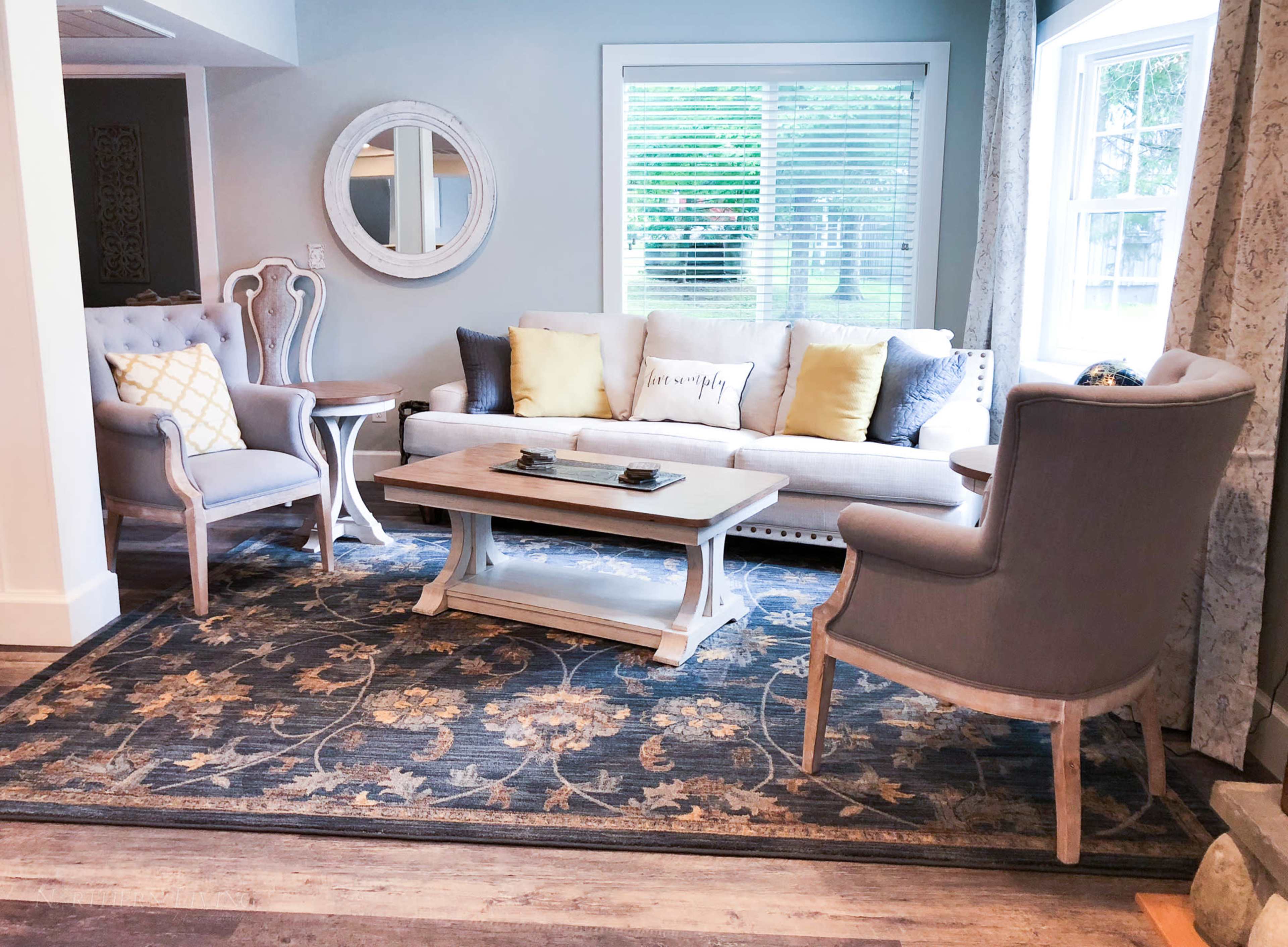 A living room with a gray sofa, two matching chairs, a coffee table, and a large area rug, all arranged around a window with natural light.