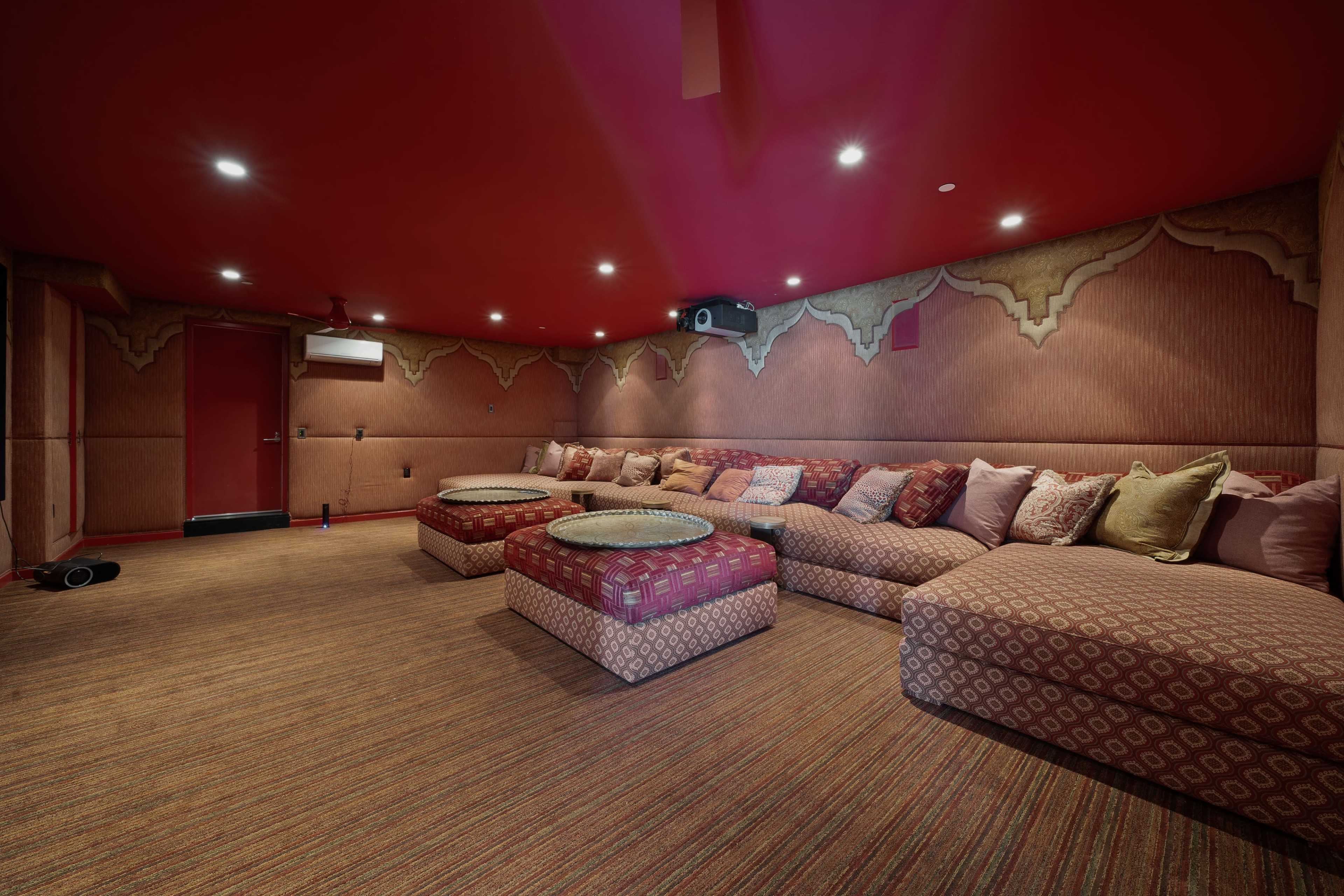 A home theater room with red walls and ceiling, featuring large cushioned seating arranged around low circular tables.