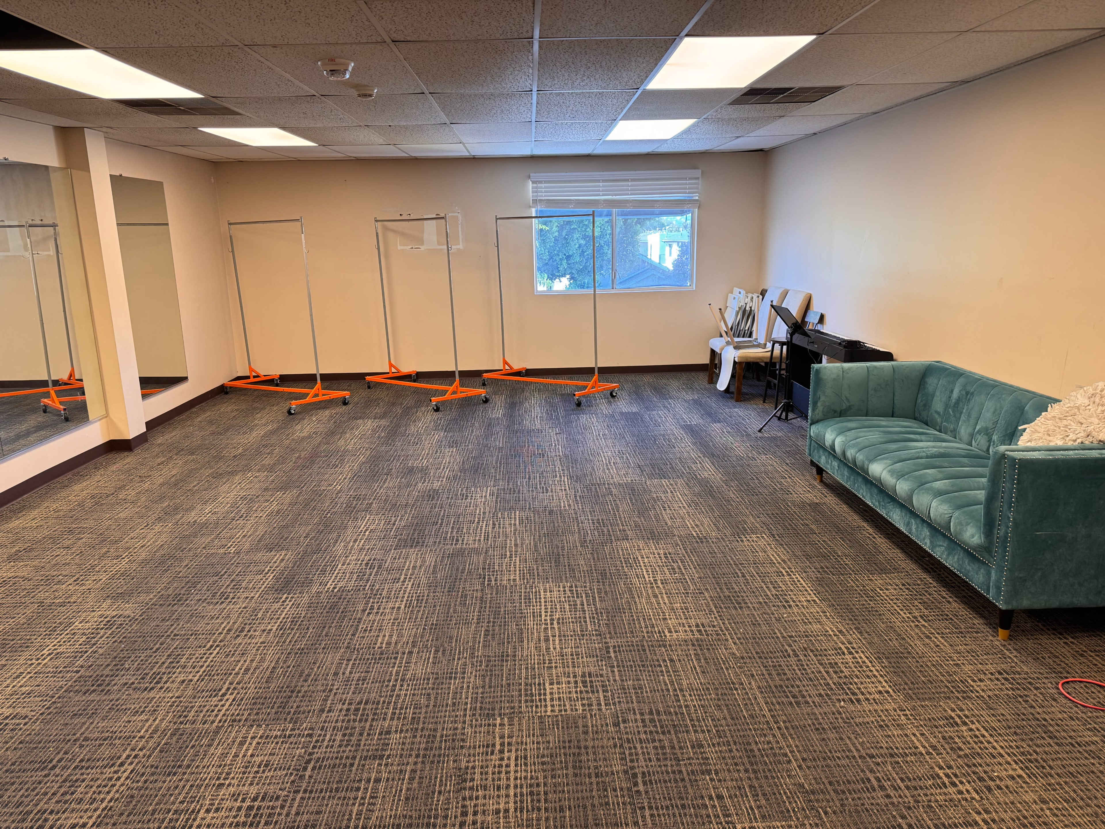 The image shows a spacious room with a blue couch, a row of clothing racks, a piano, and a mirror on one wall.