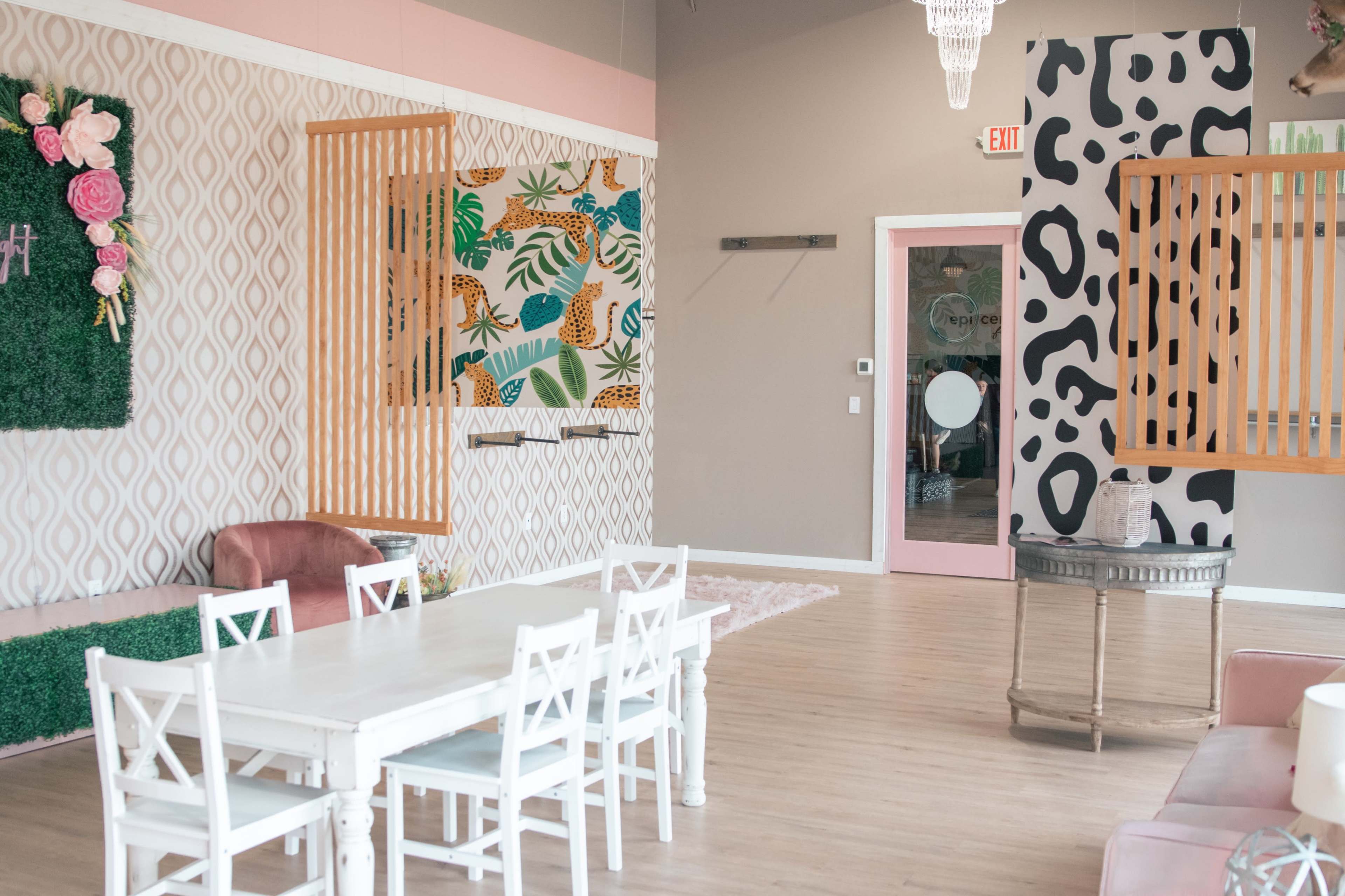 A brightly lit interior features a white dining table with chairs, patterned wallpaper, and decorative wall panels.