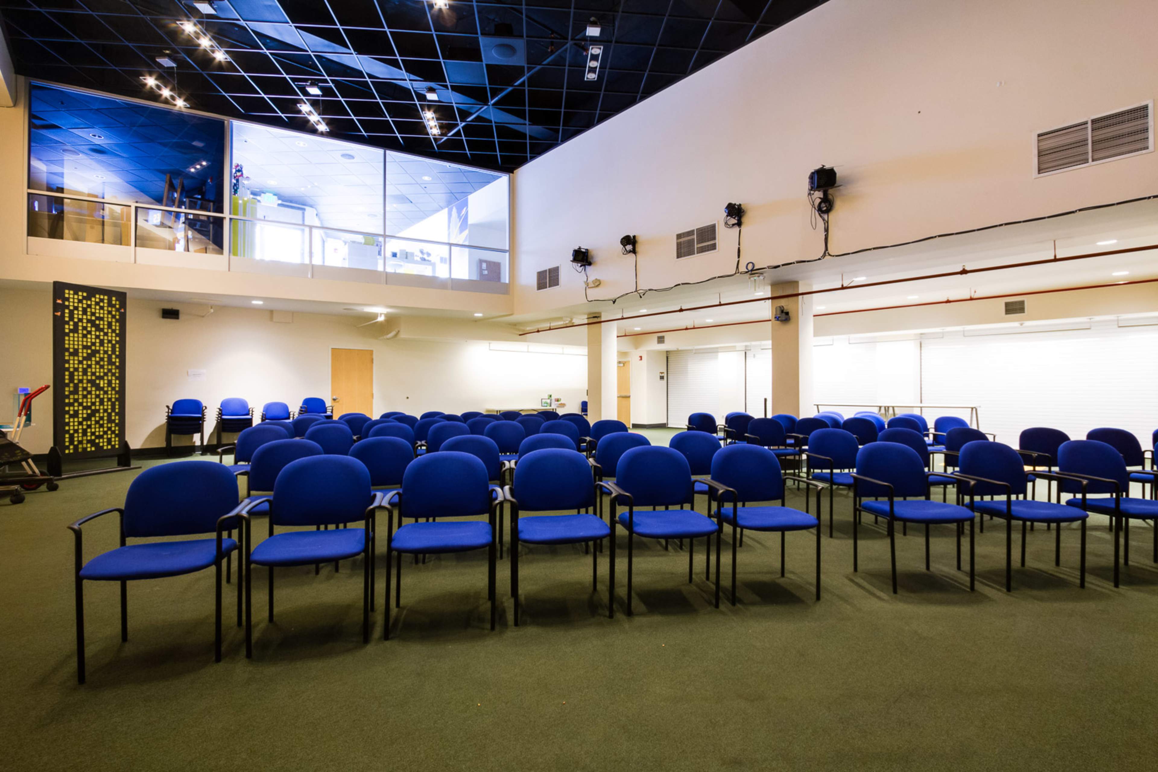 Empty blue chairs are arranged in rows in a well-lit conference room.