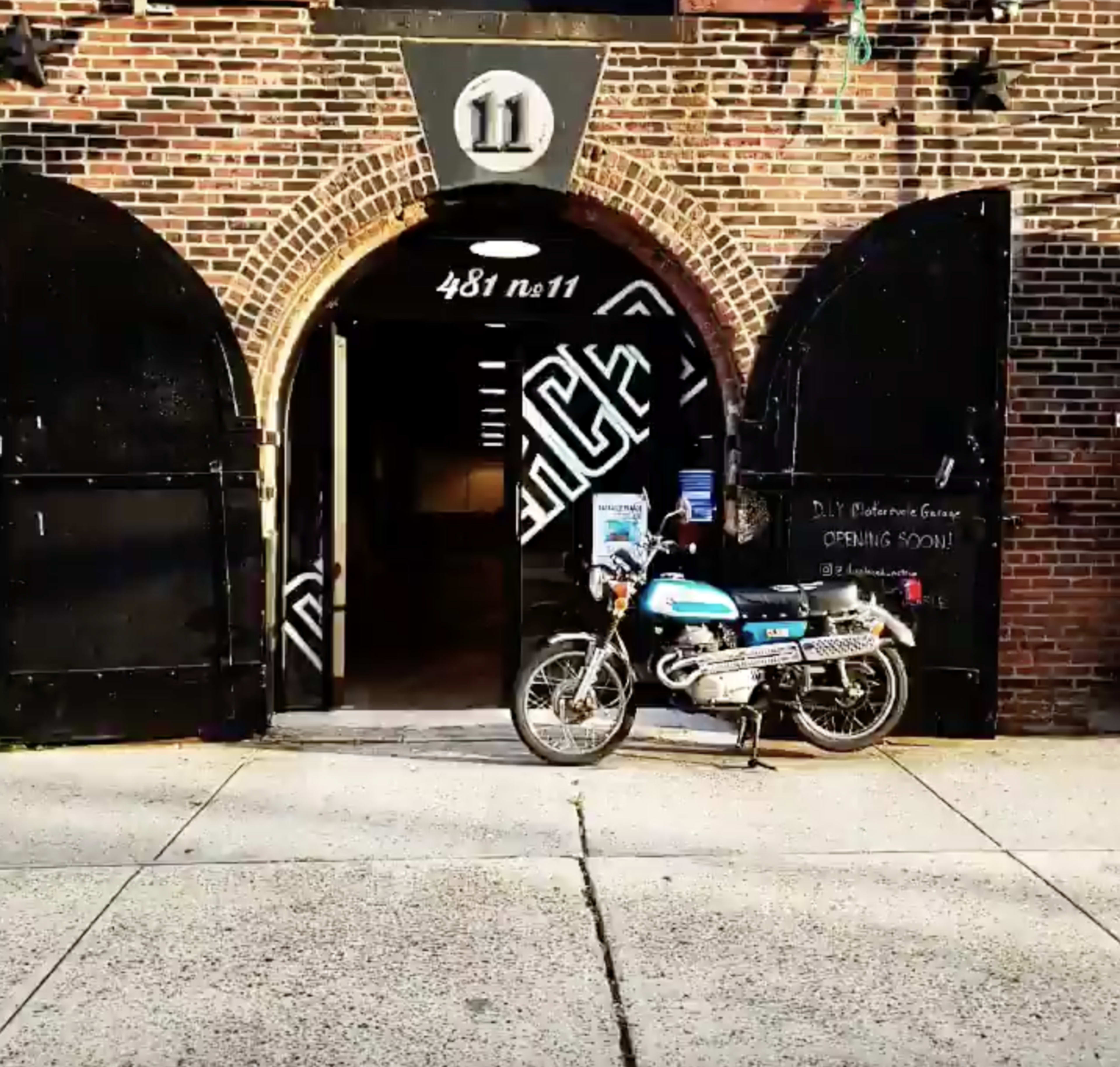 A blue and silver motorcycle is parked outside a large arched doorway marked with the number 11, set within a brick wall.