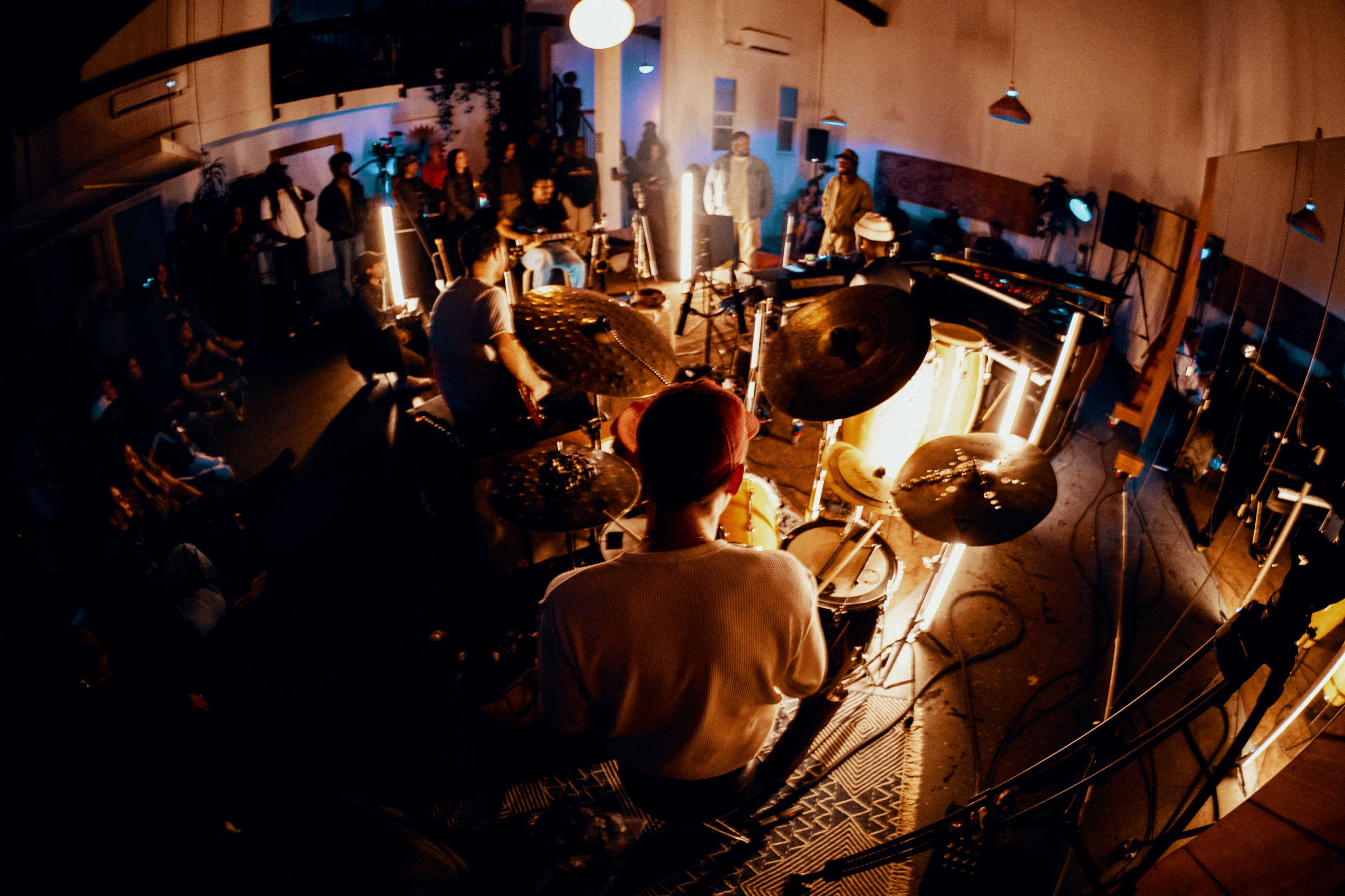 A band performs on stage in a dimly lit room filled with an audience.