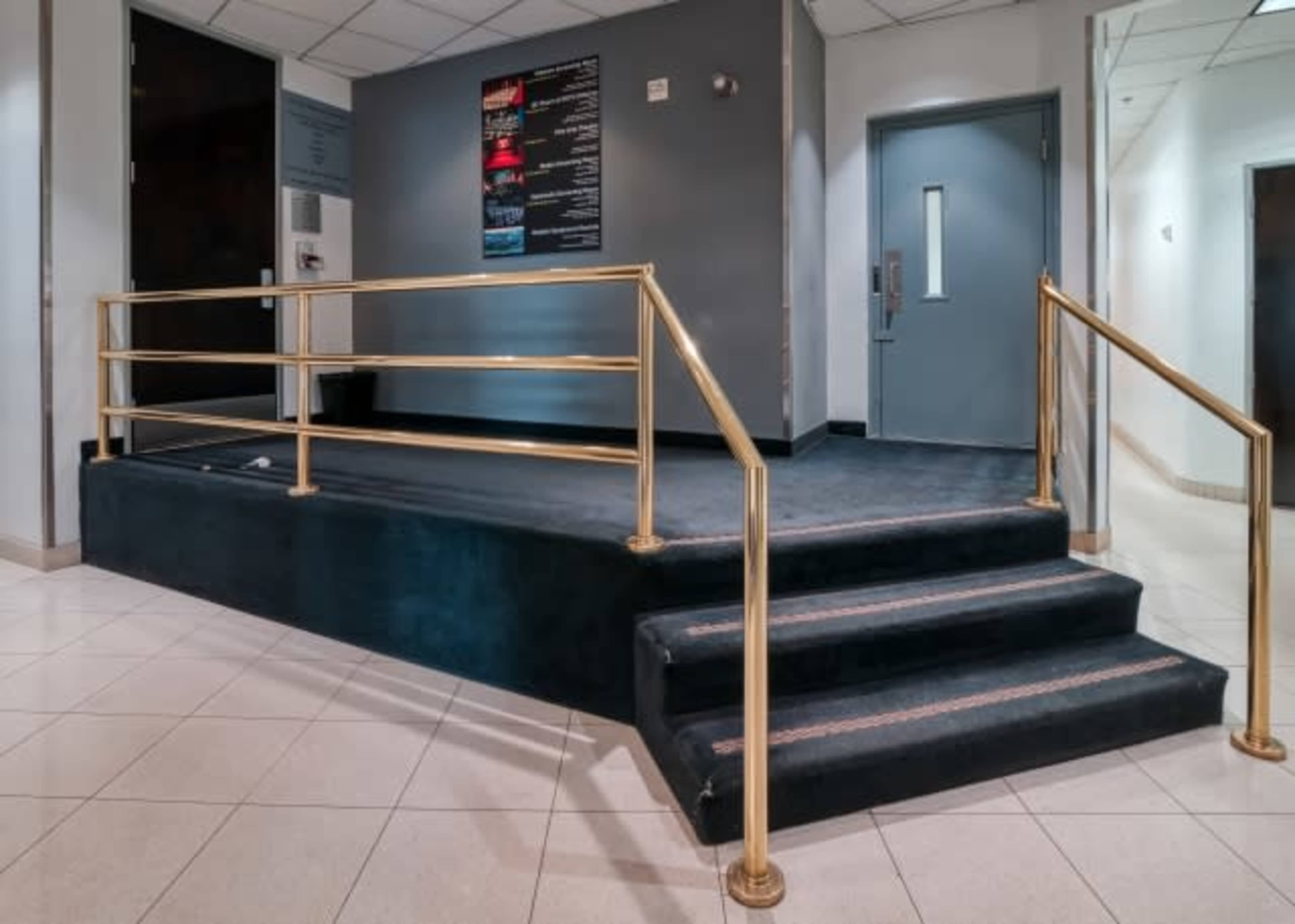 The image shows a small set of steps with a gold railing leading up to a platform in a hallway.