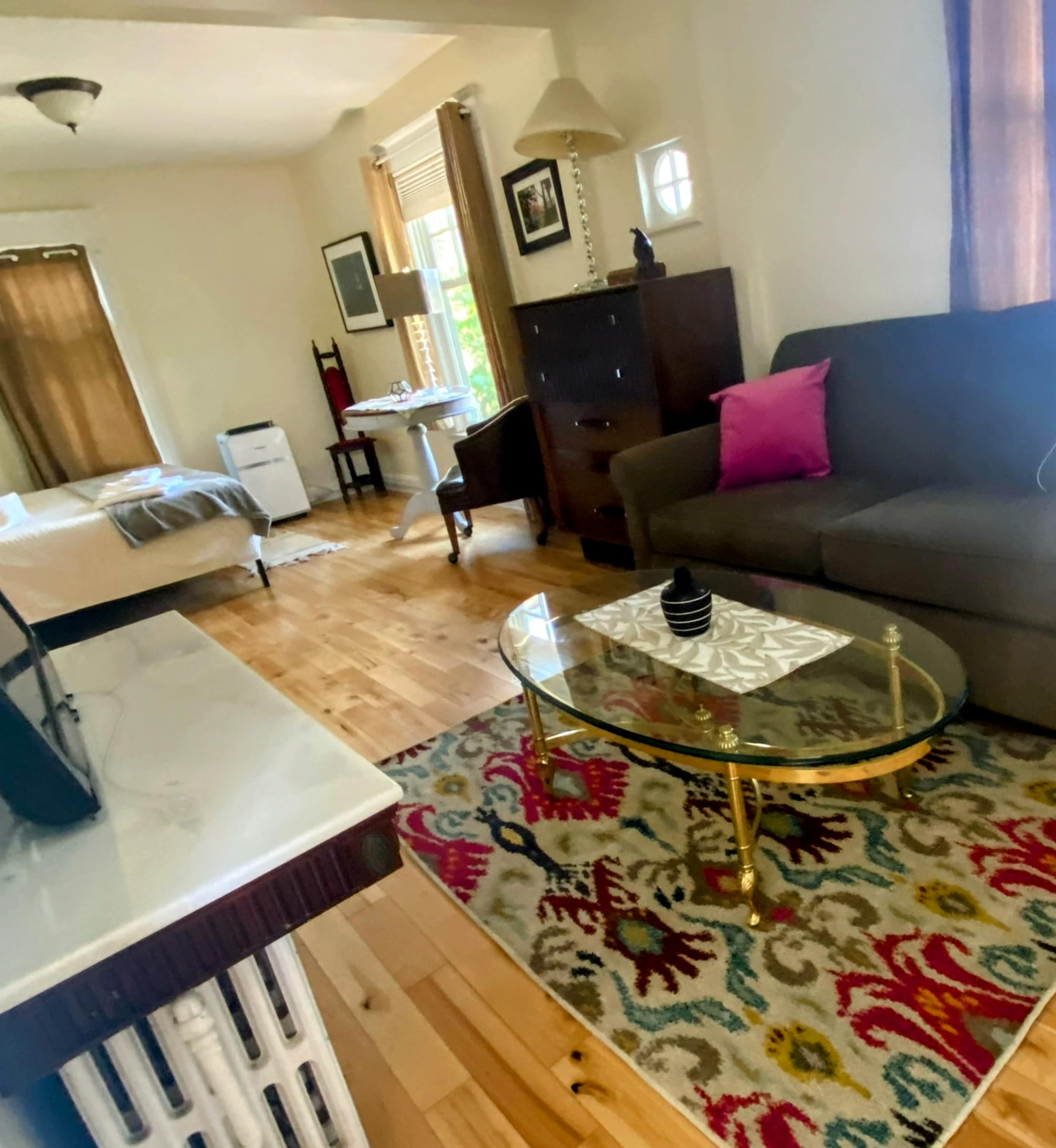 The image shows a cozy living room with a sofa, a table, and a decorative rug, along with a bed visible in the background.