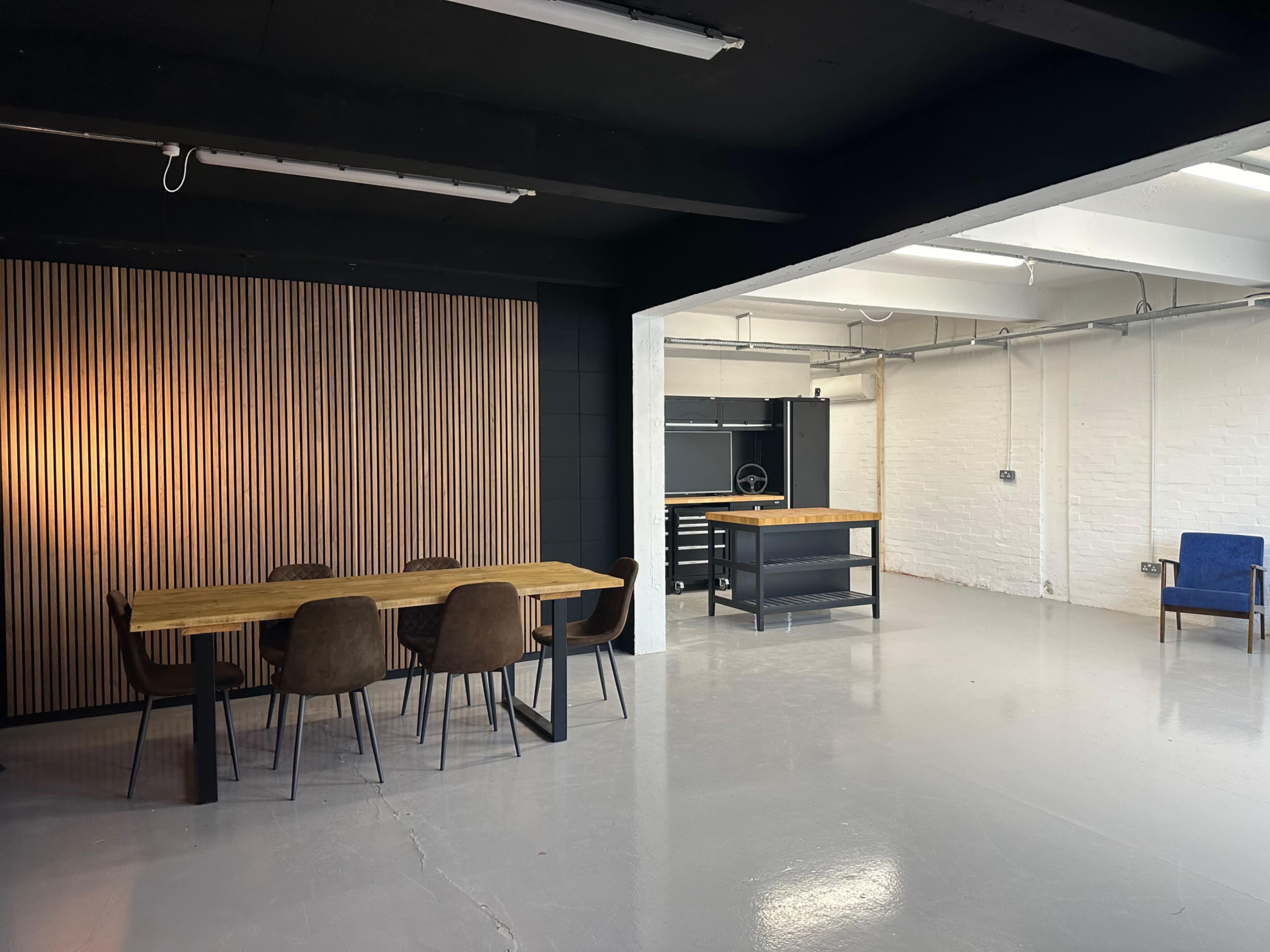 A spacious industrial-style room with a wooden dining table, chairs, and a separate workbench area.