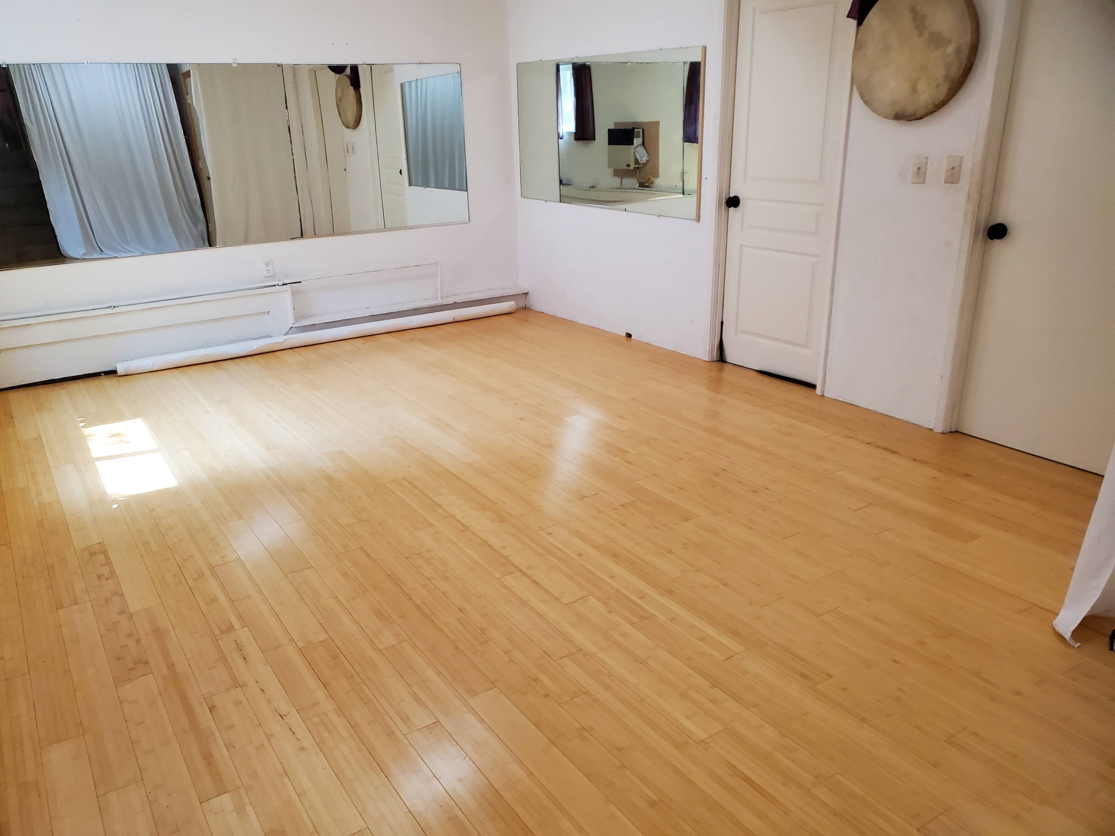 An empty room with bamboo flooring, two mirrors on the wall, and a door leading to another space.
