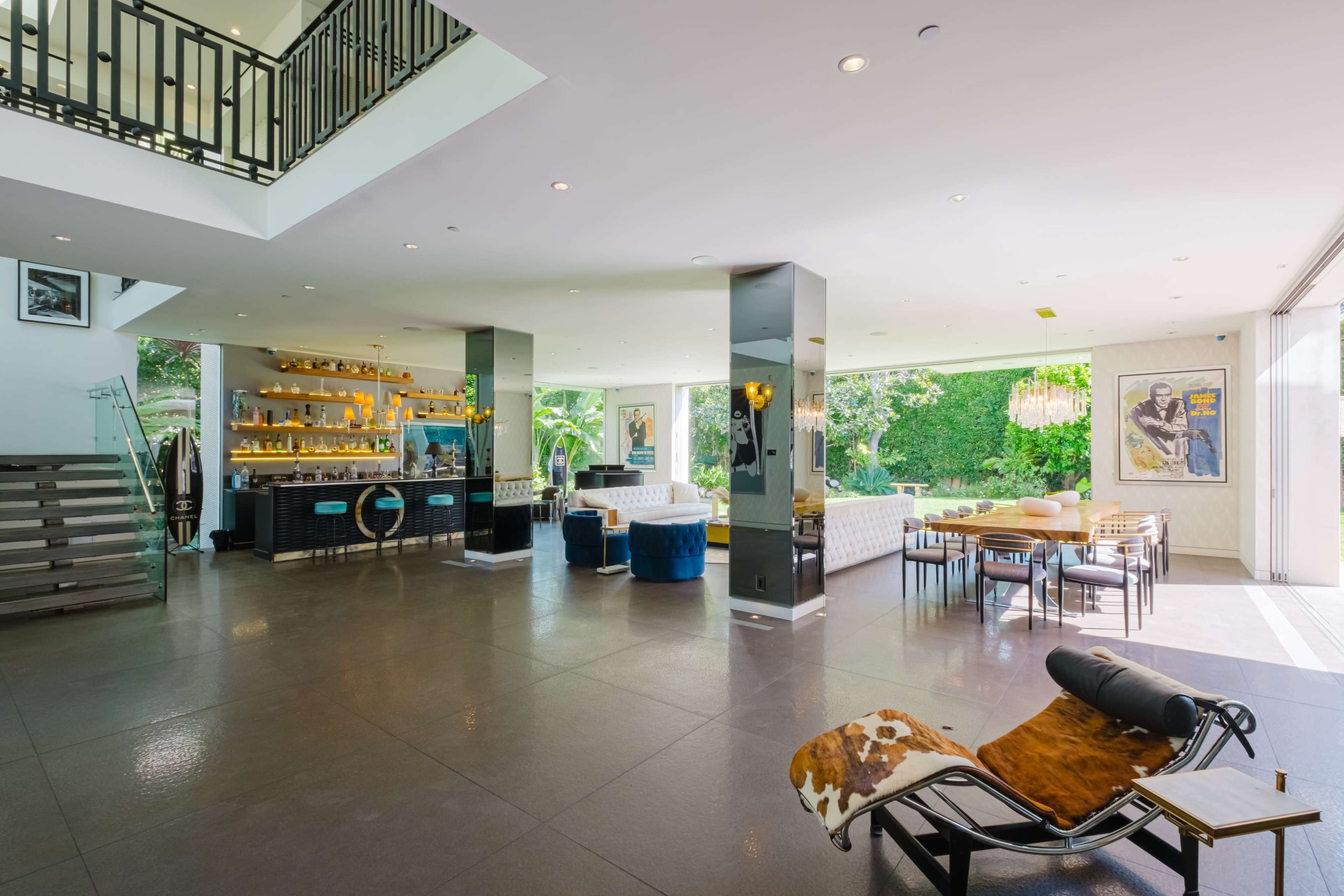 A spacious, modern interior of a home featuring an open living area with a kitchen, dining space, and lounge, surrounded by large windows and greenery.