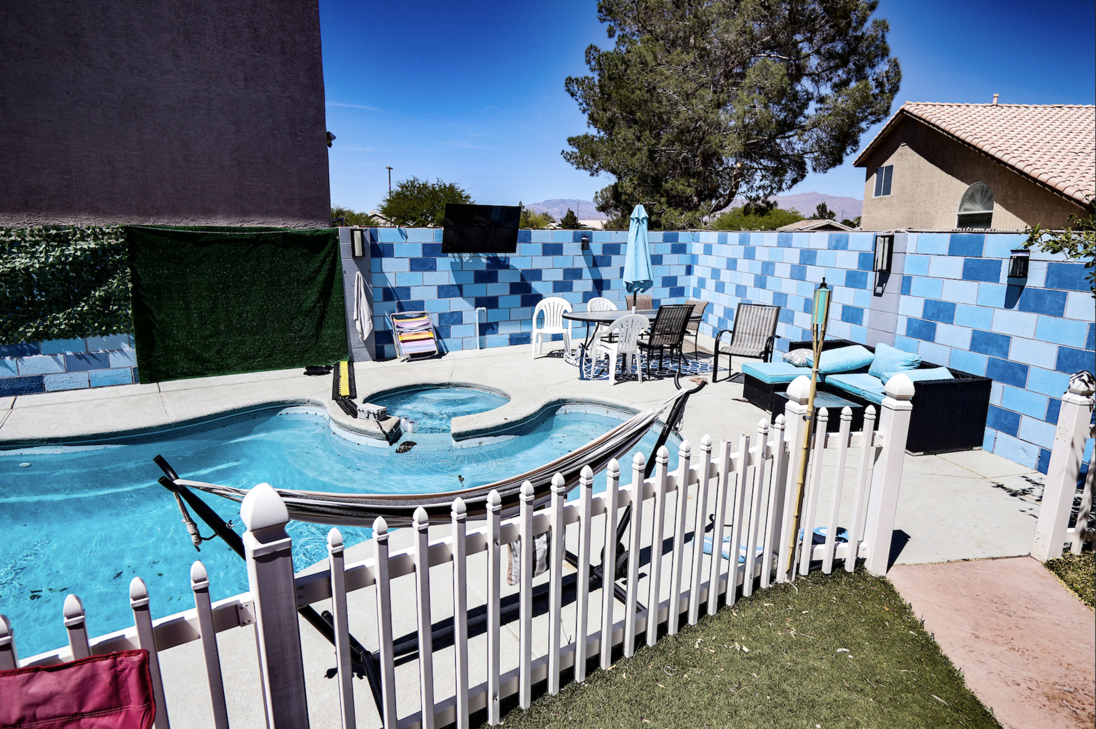 The image shows a backyard swimming pool area with a hammock, patio furniture, and a fence surrounding the pool.