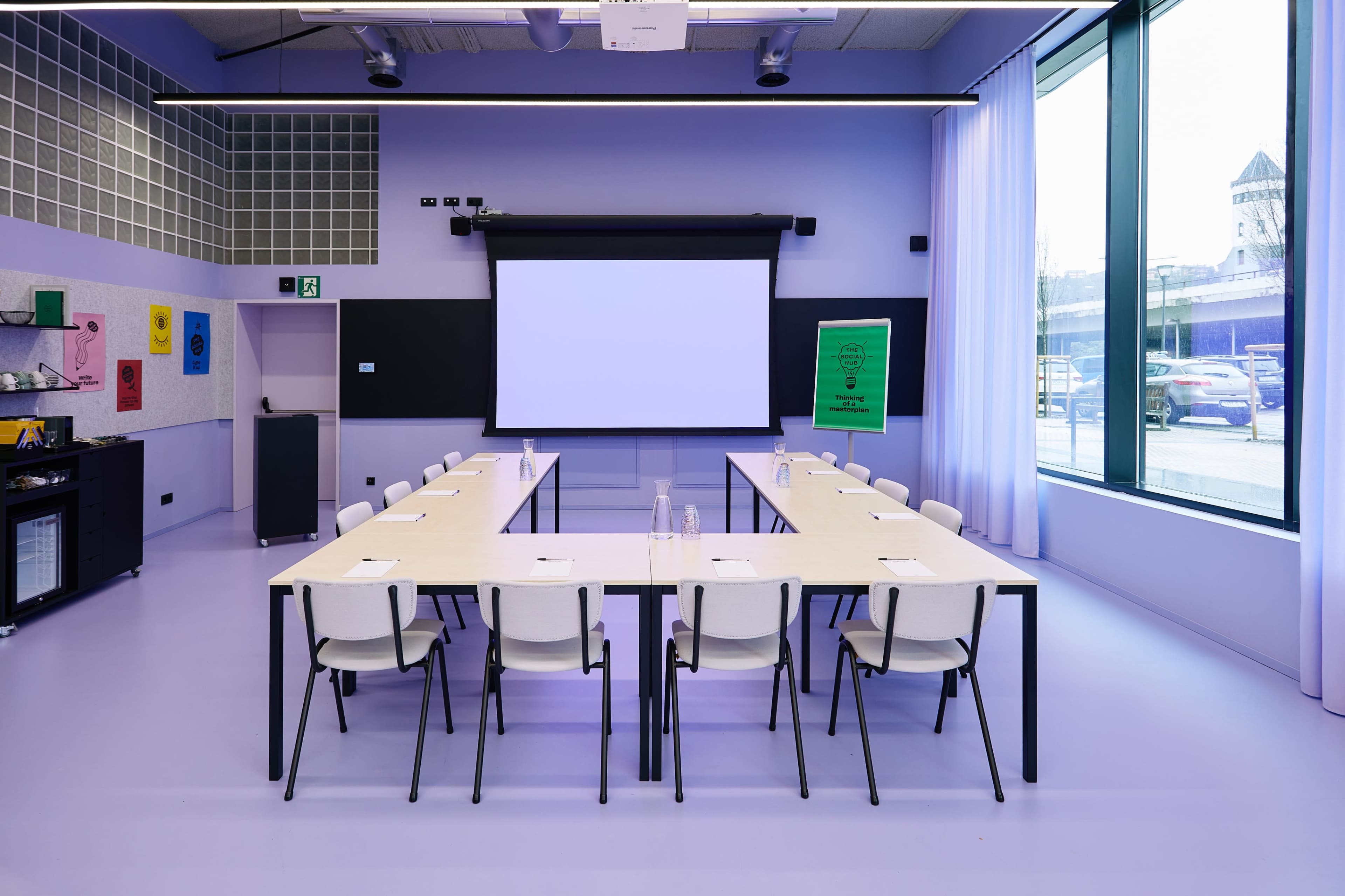 A modern conference room features a long table with chairs, a projector screen, and large windows.
