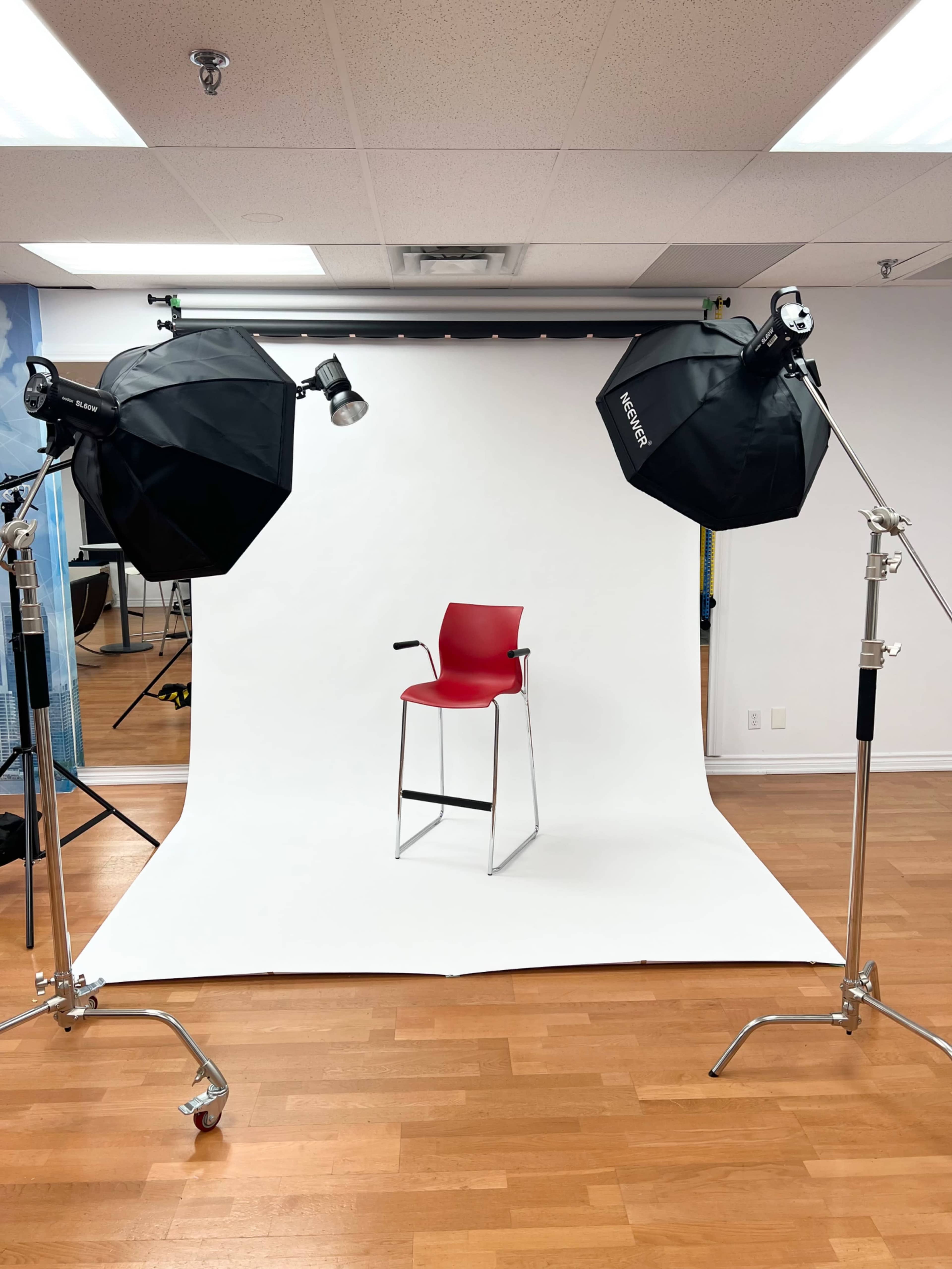 A red chair is positioned on a white backdrop surrounded by two softbox lights in a studio setting.