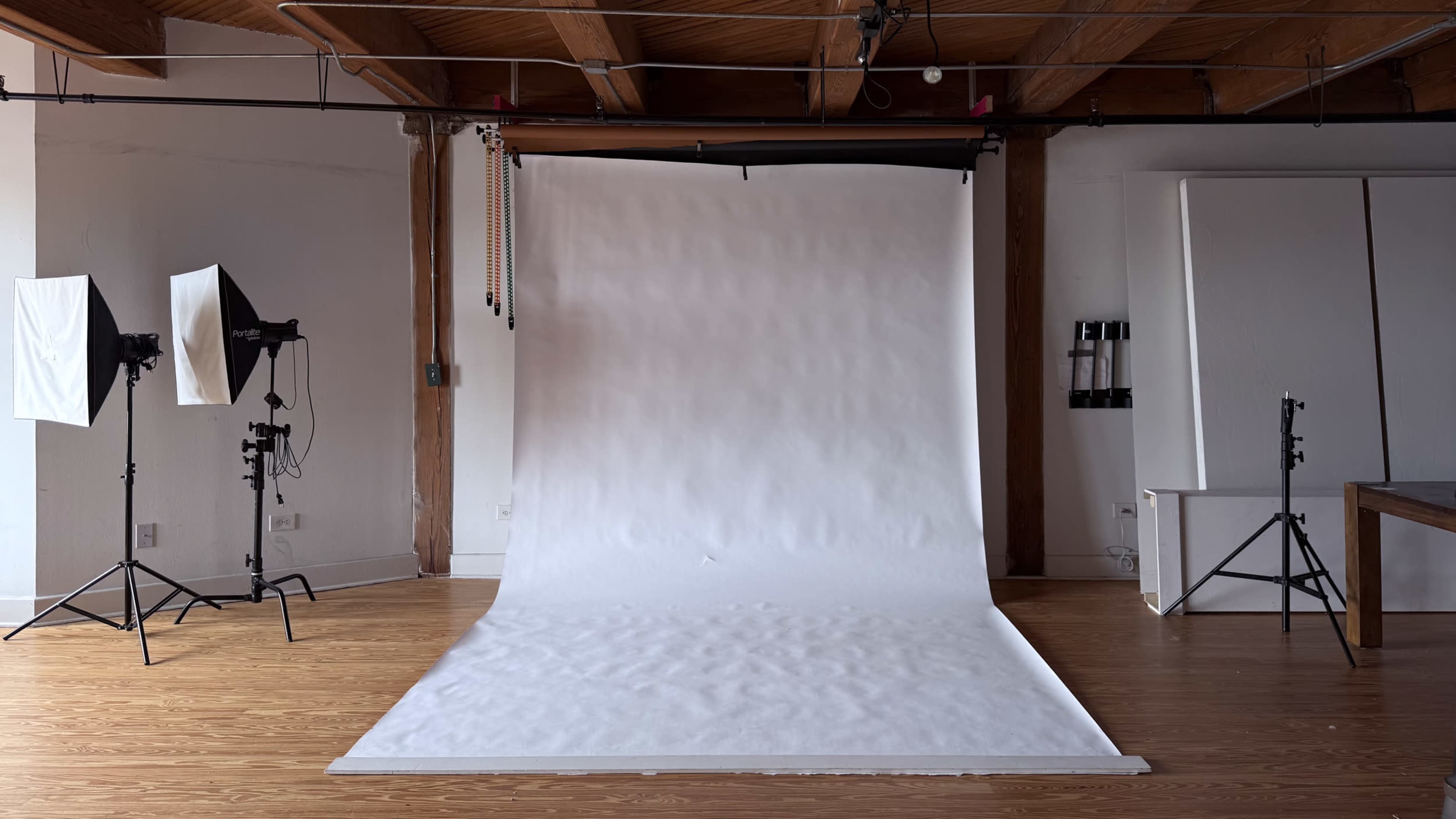 The image shows a photography studio with a large white backdrop and two softbox lighting setups on either side.