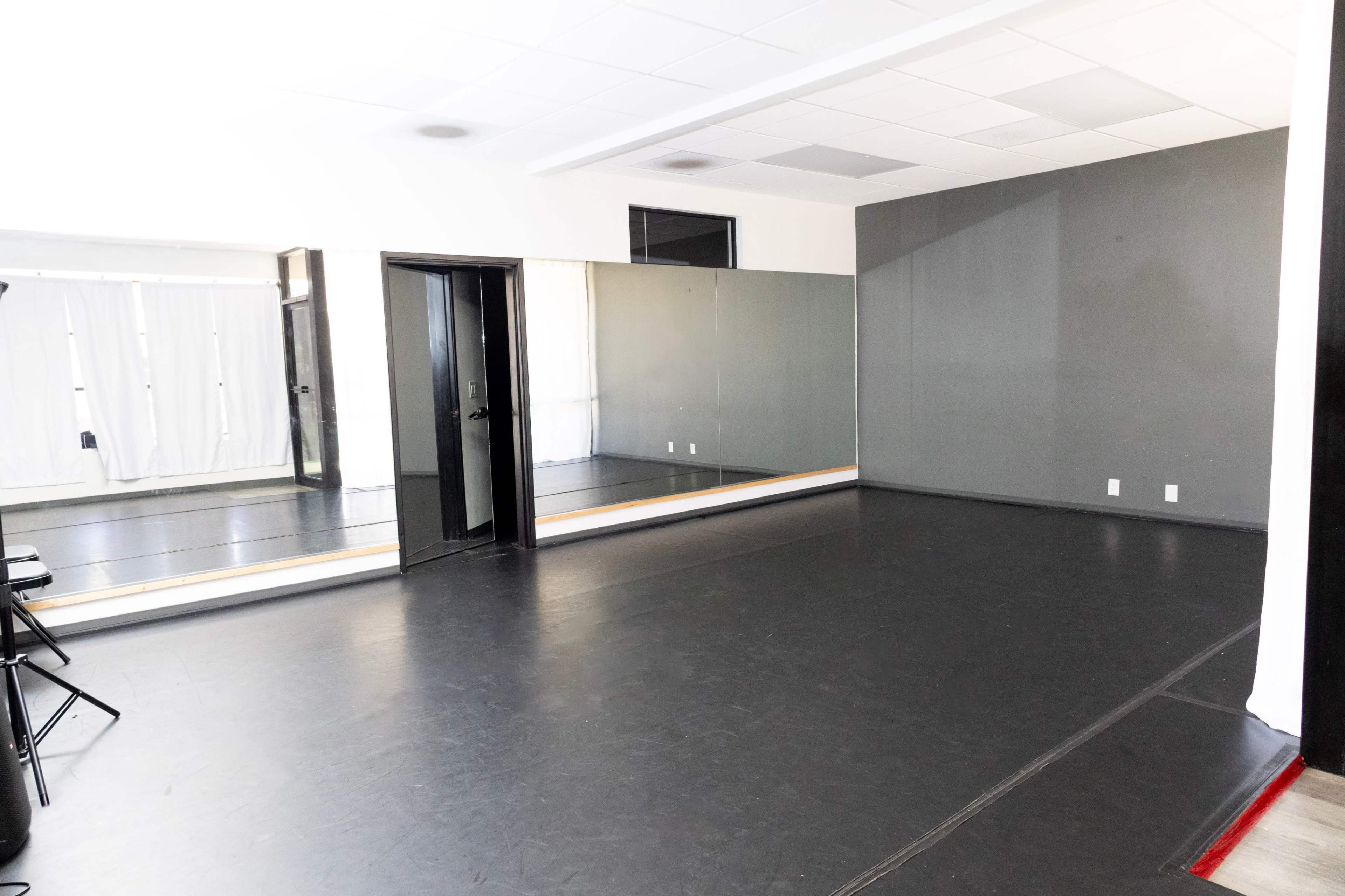 The image shows a spacious dance studio with a large mirror on one wall and a smooth black floor.
