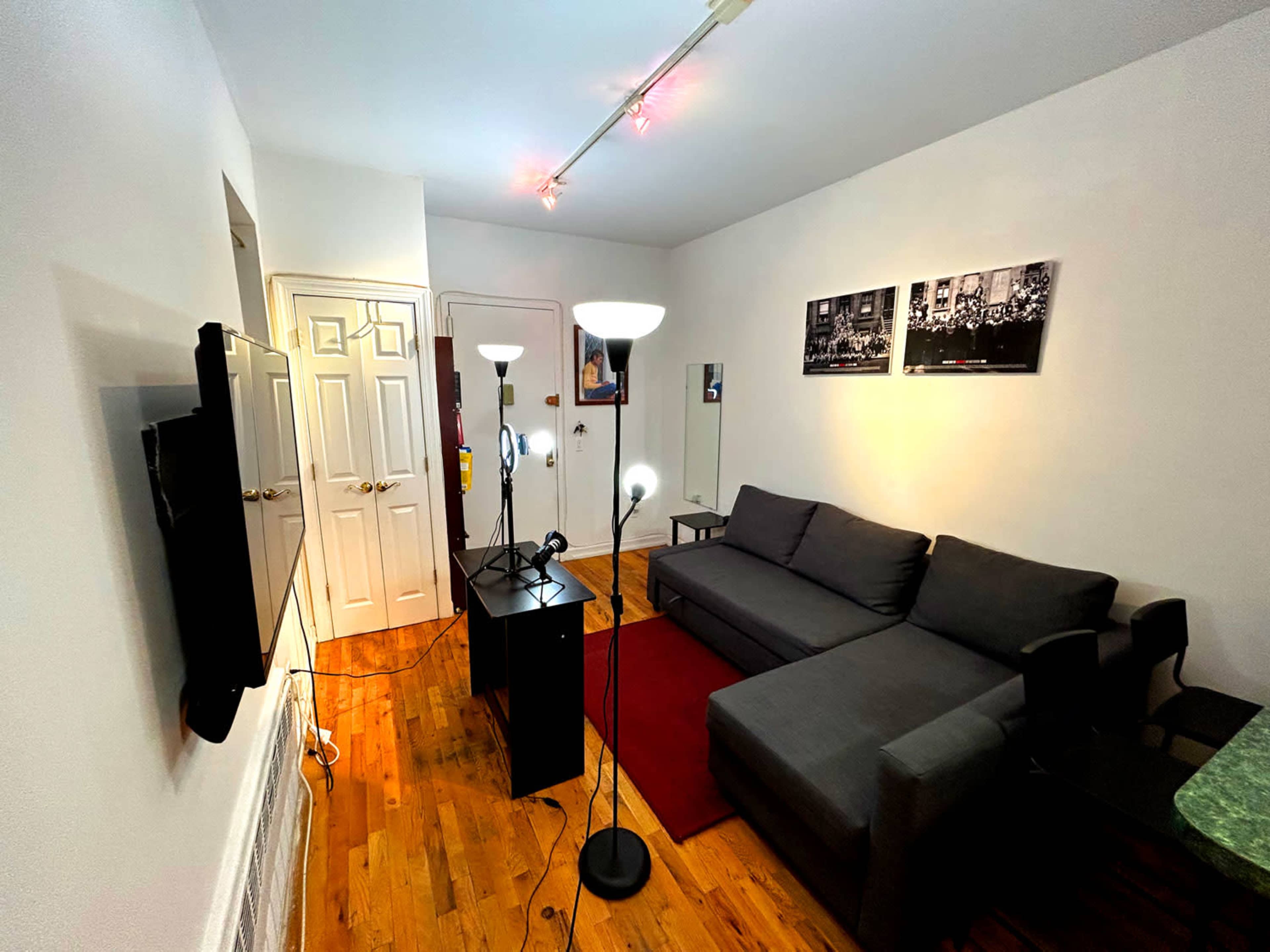 A living room with a gray sofa, two standing lamps, a television mounted on the wall, and wooden flooring.
