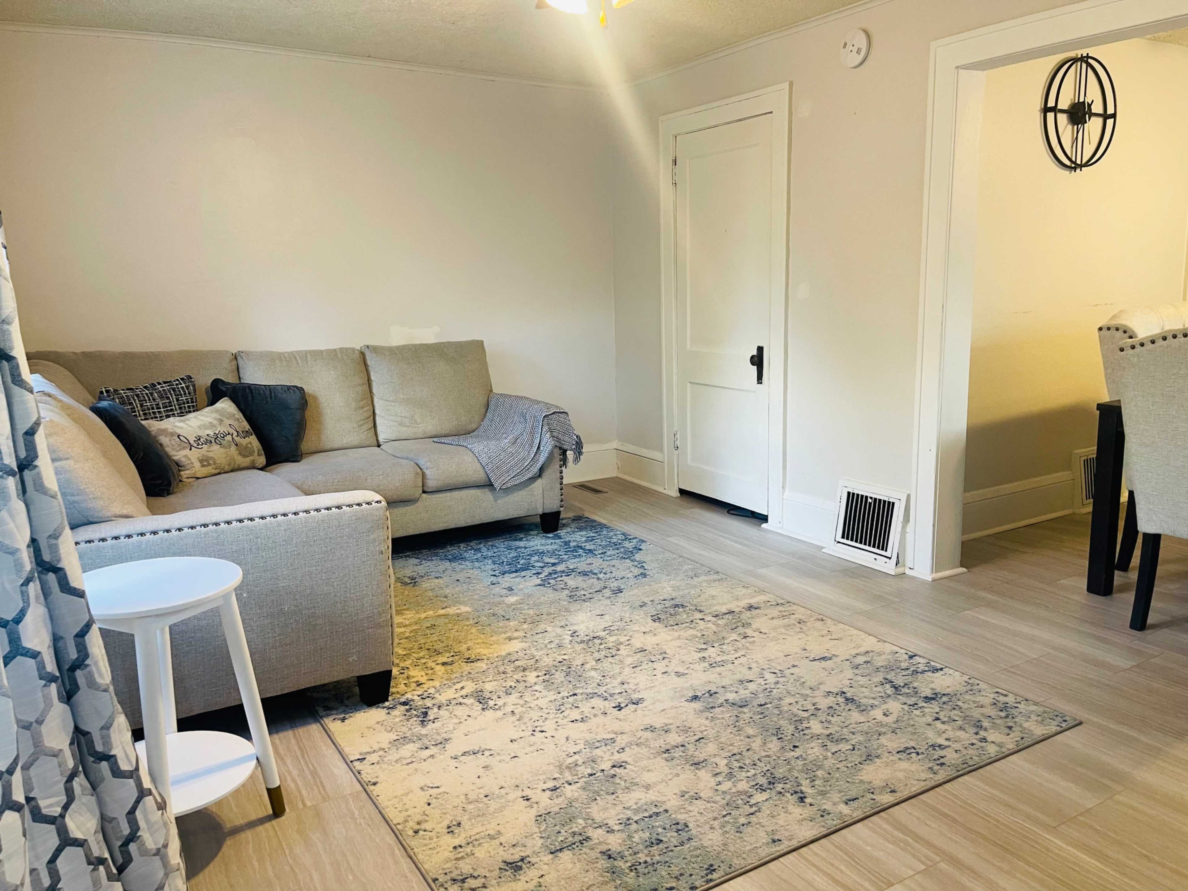 A light-colored living room with a beige sofa, a patterned area rug, and a small side table next to the sofa.