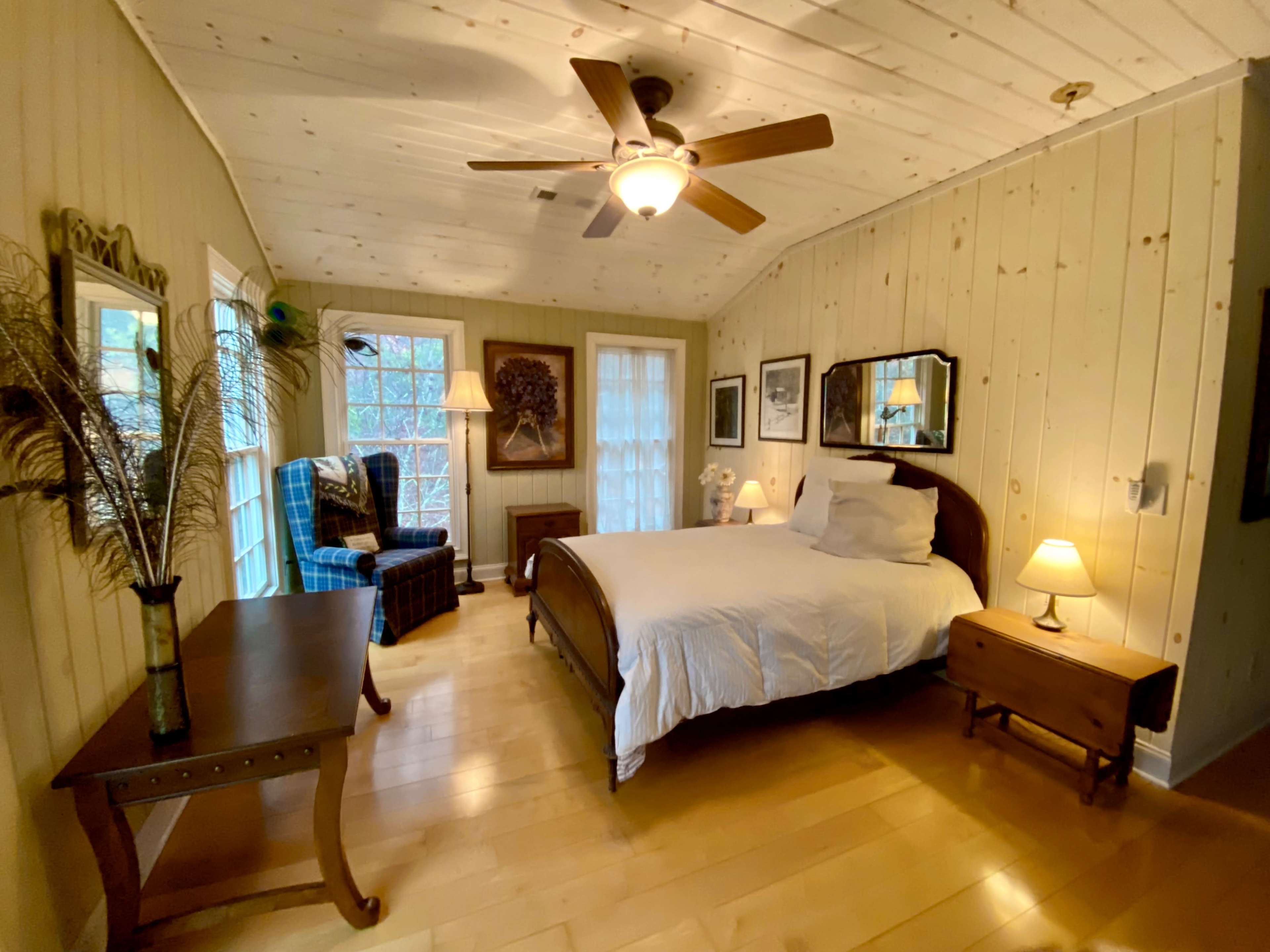 A cozy bedroom featuring a wooden bed, a side table with a lamp, a dresser, and a comfortable armchair near a window.