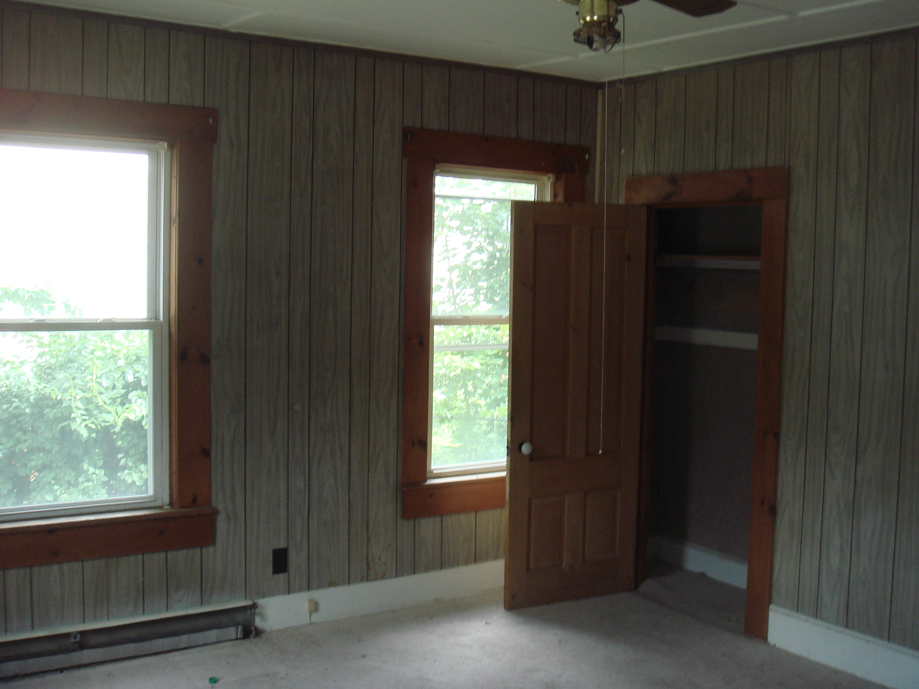 A sparsely furnished room with wooden paneling, two windows, and a door leading to a small closet.