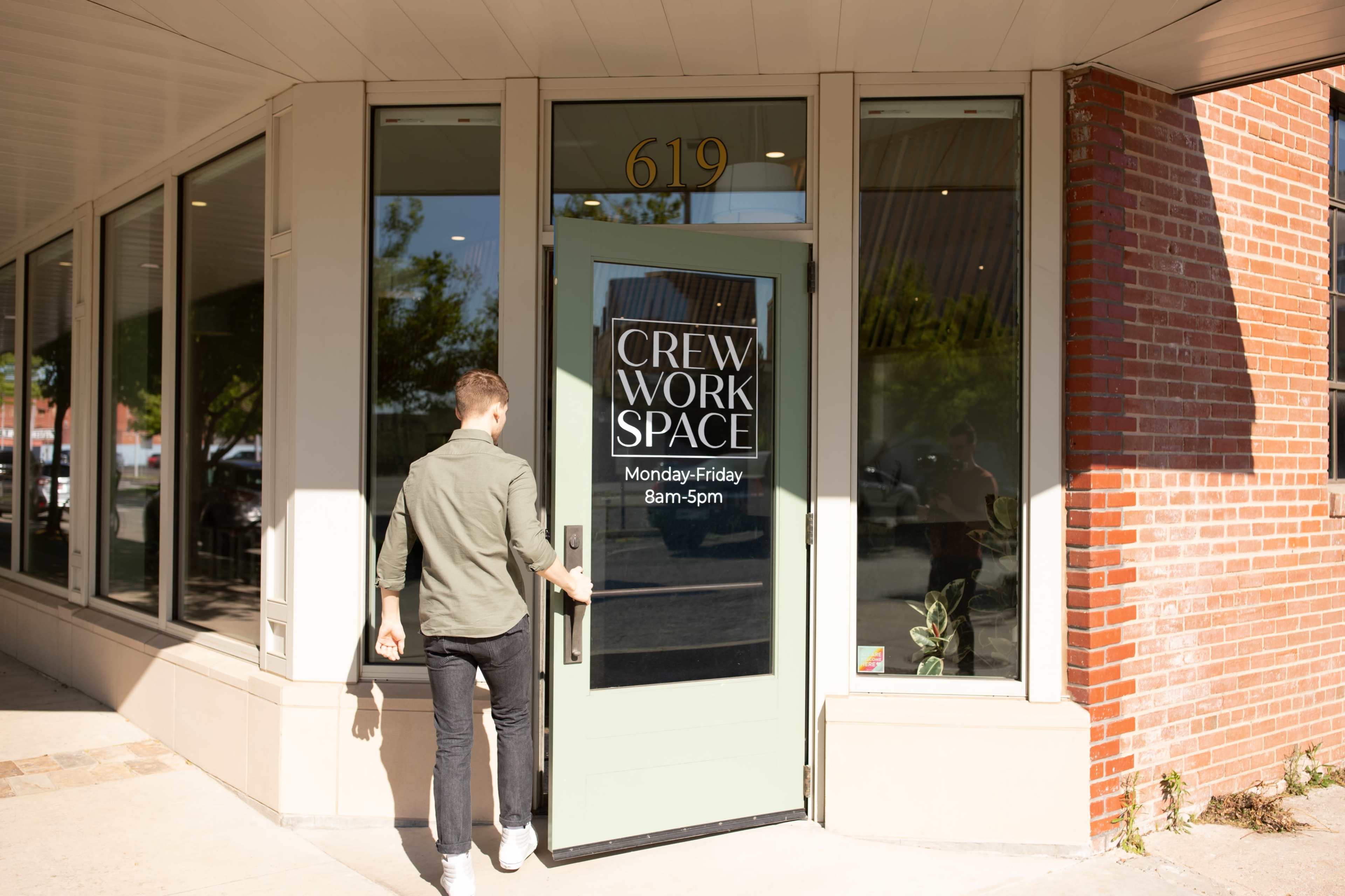 A person is entering a workspace through a glass door that has a sign indicating the hours of operation.