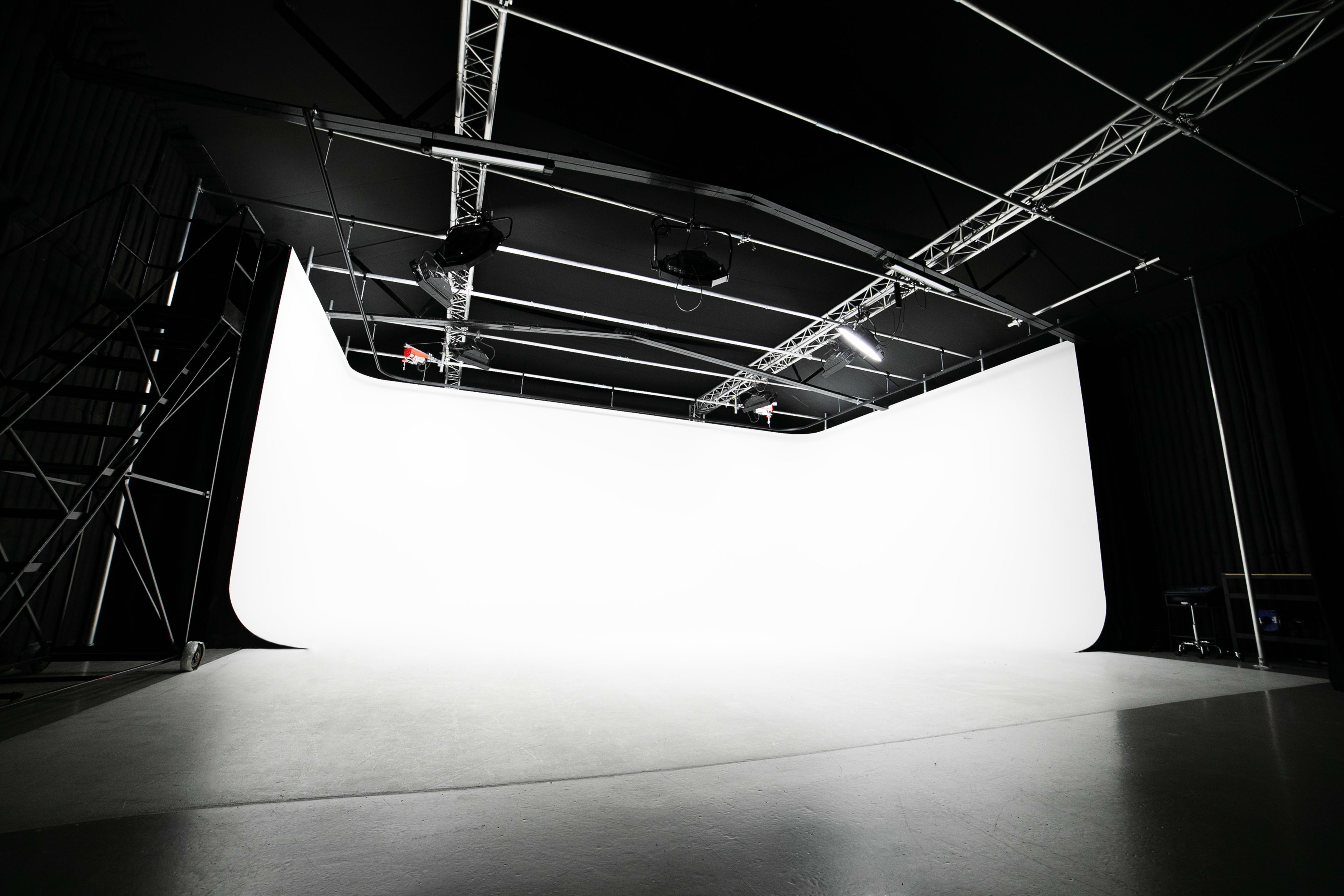 The image shows an empty photography studio with a large white backdrop and overhead lighting.