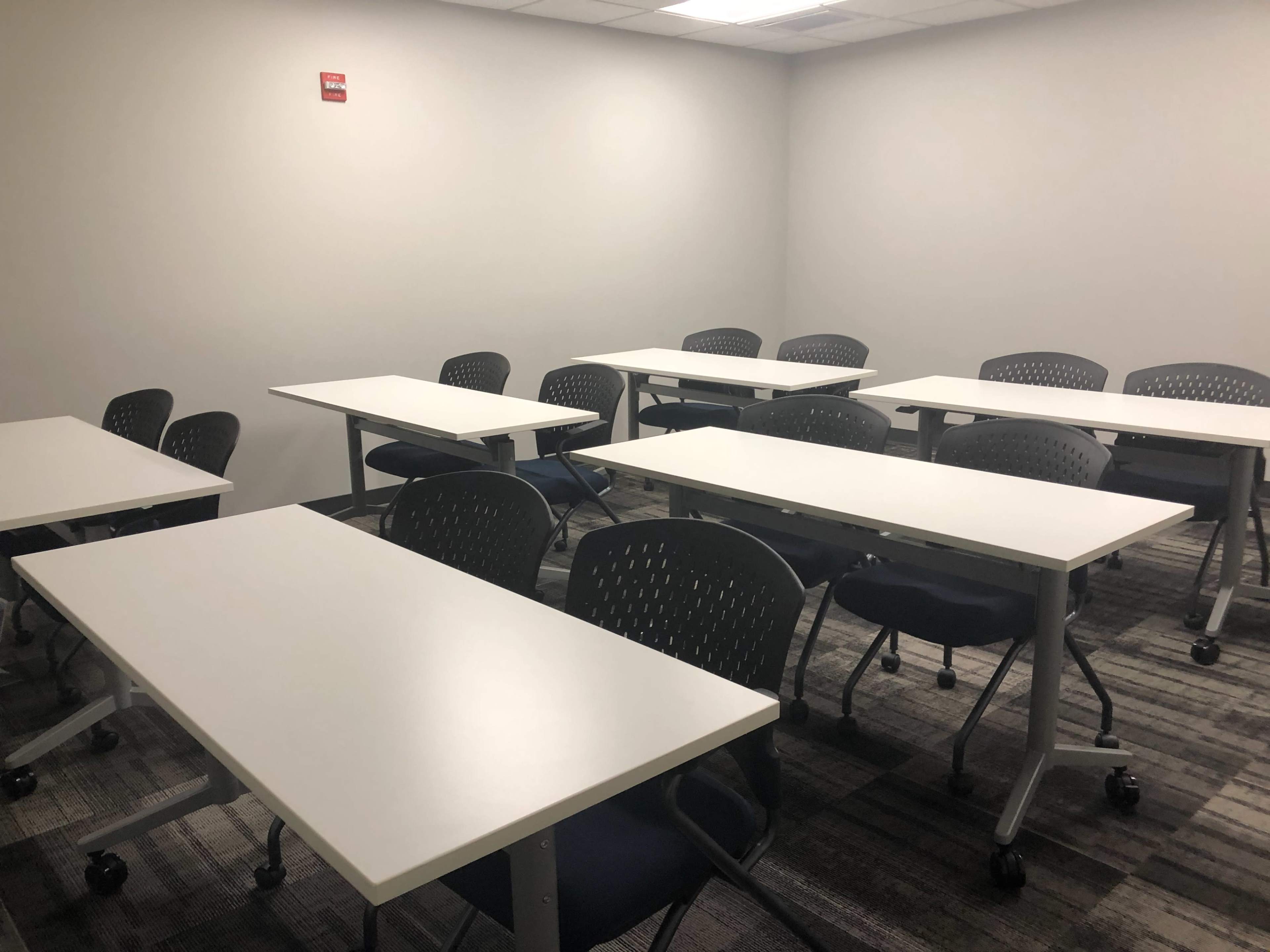 A classroom with multiple tables and chairs arranged in a sparse layout.