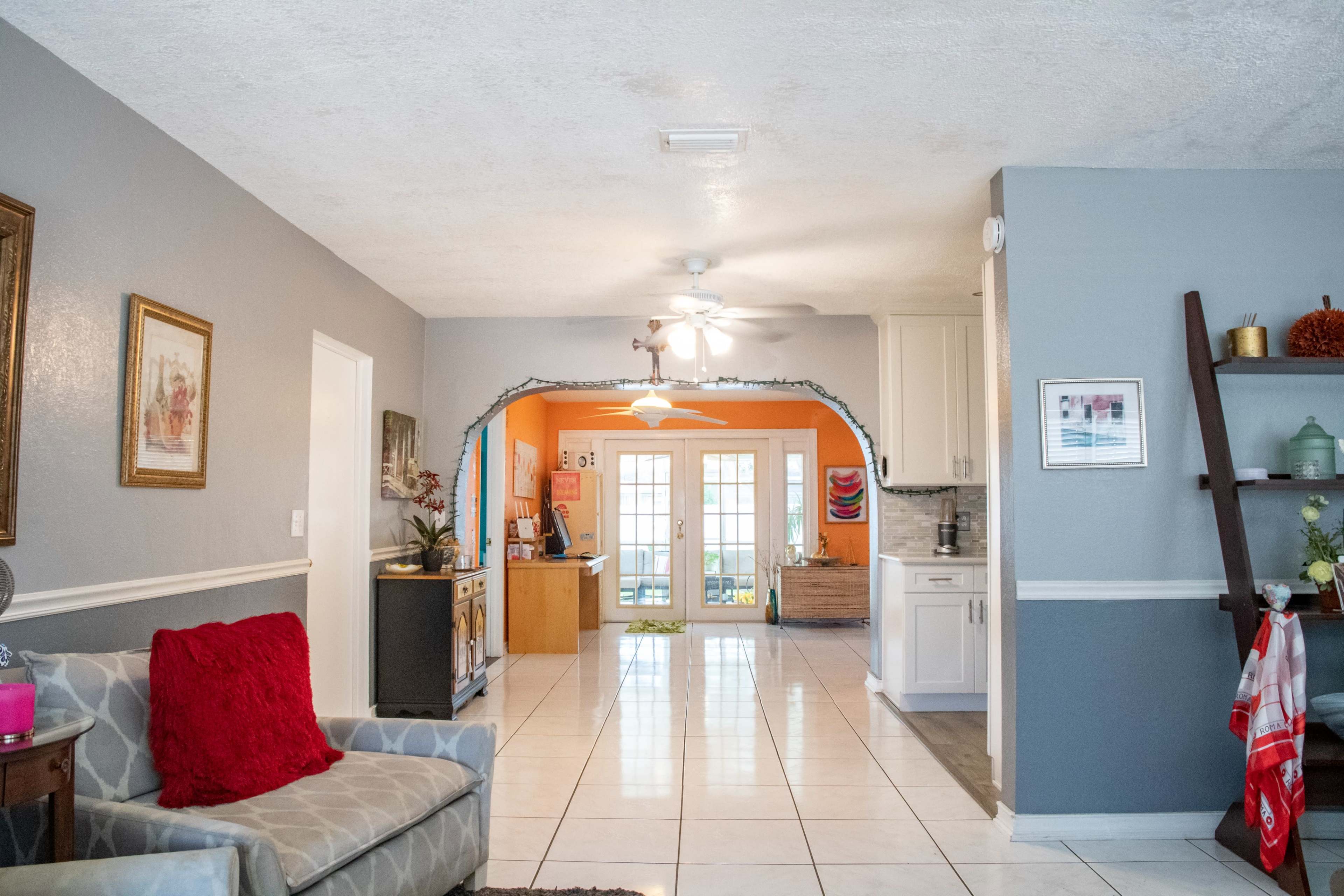 A living room with a view into a brightly colored kitchen and dining area, featuring tile flooring and an archway between the two spaces.
