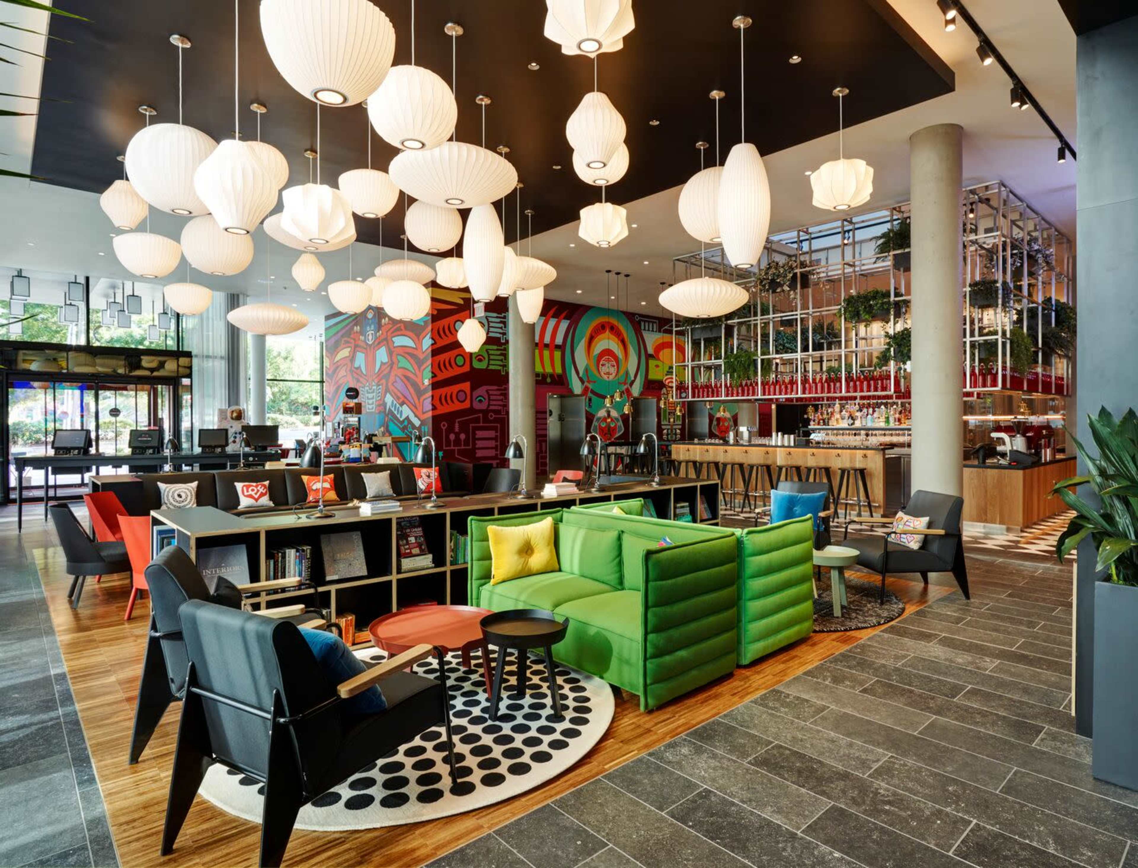 A modern lobby features colorful furnishings, unique light fixtures, and a vibrant wall mural.