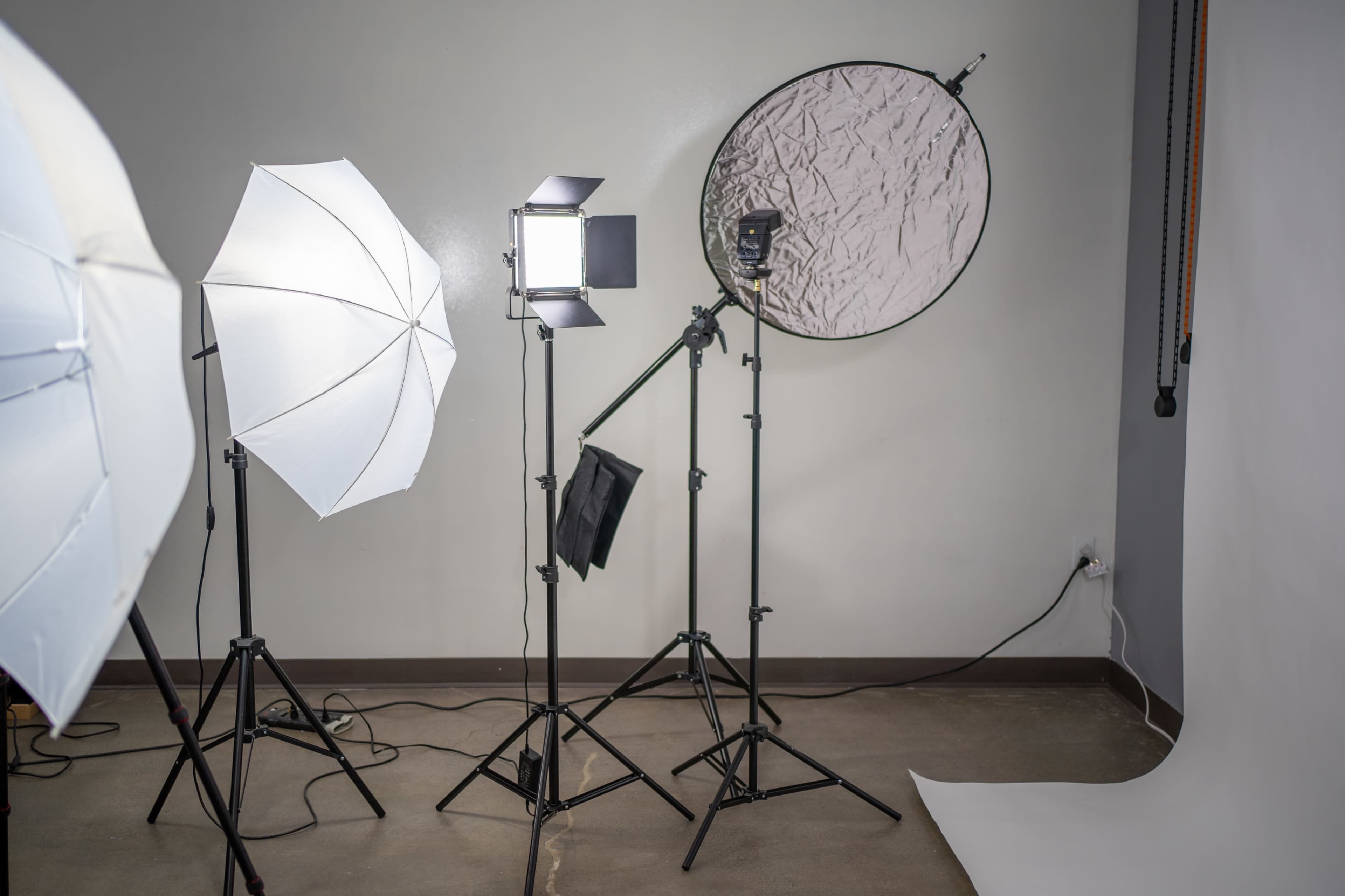 A photography studio setup with various lighting equipment, including umbrella lights and a softbox, positioned around a blank backdrop.