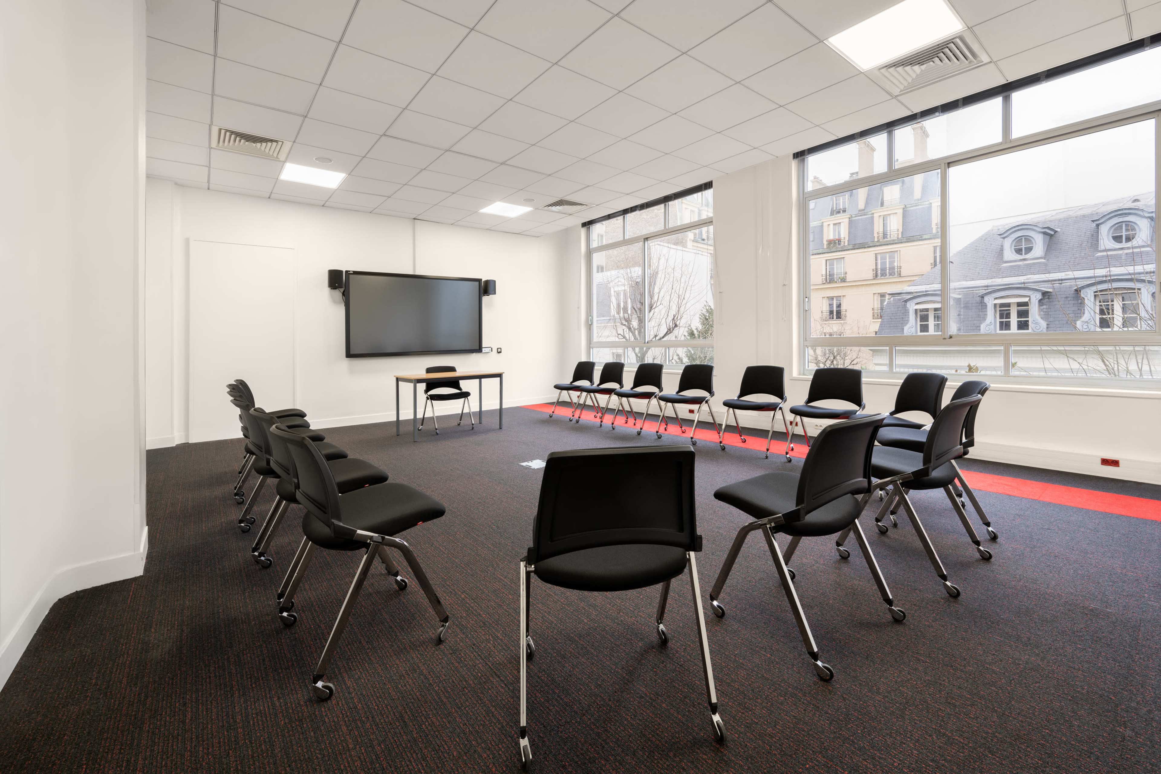 A meeting room is set up with chairs arranged in a circle facing a wall-mounted screen.