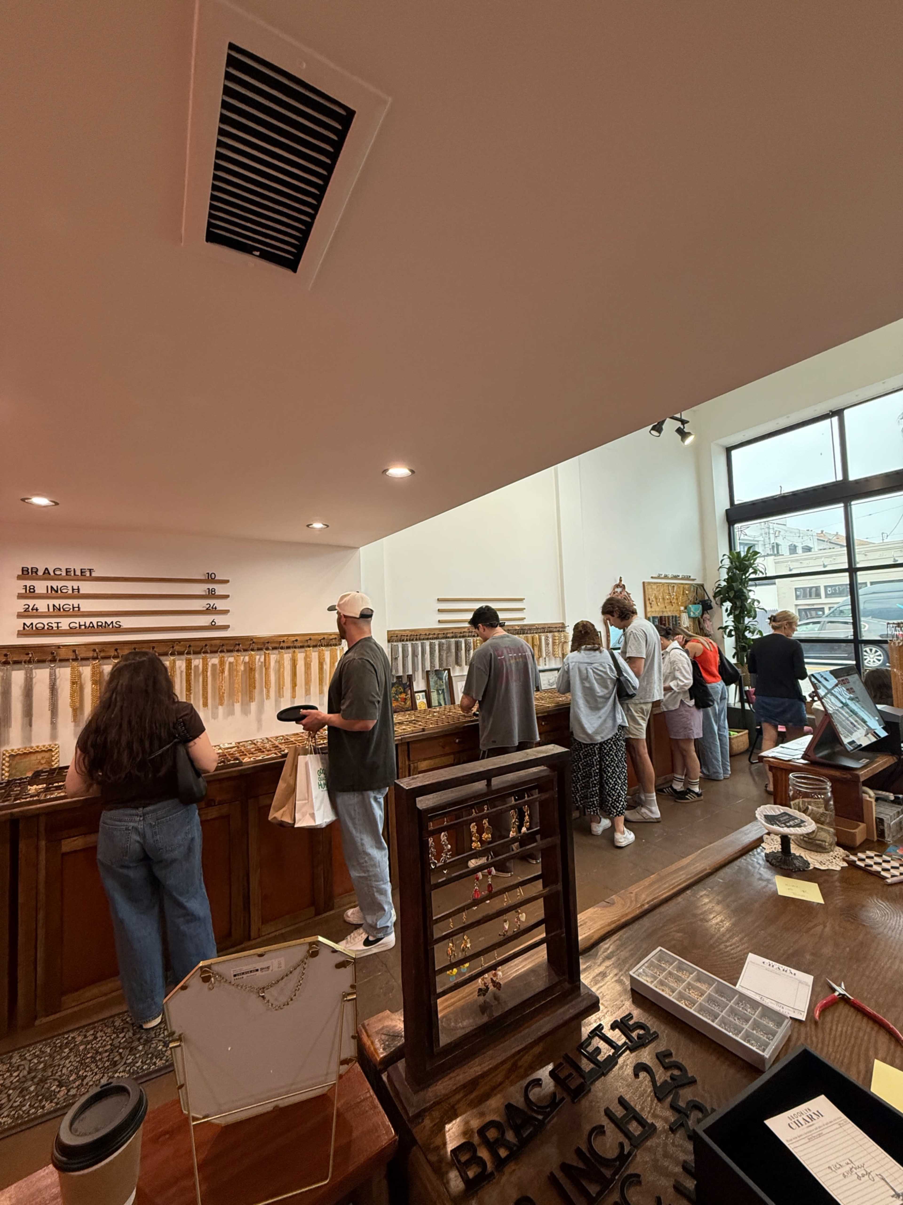 A group of people stands in a jewelry store, browsing various items displayed along a wooden counter and walls.