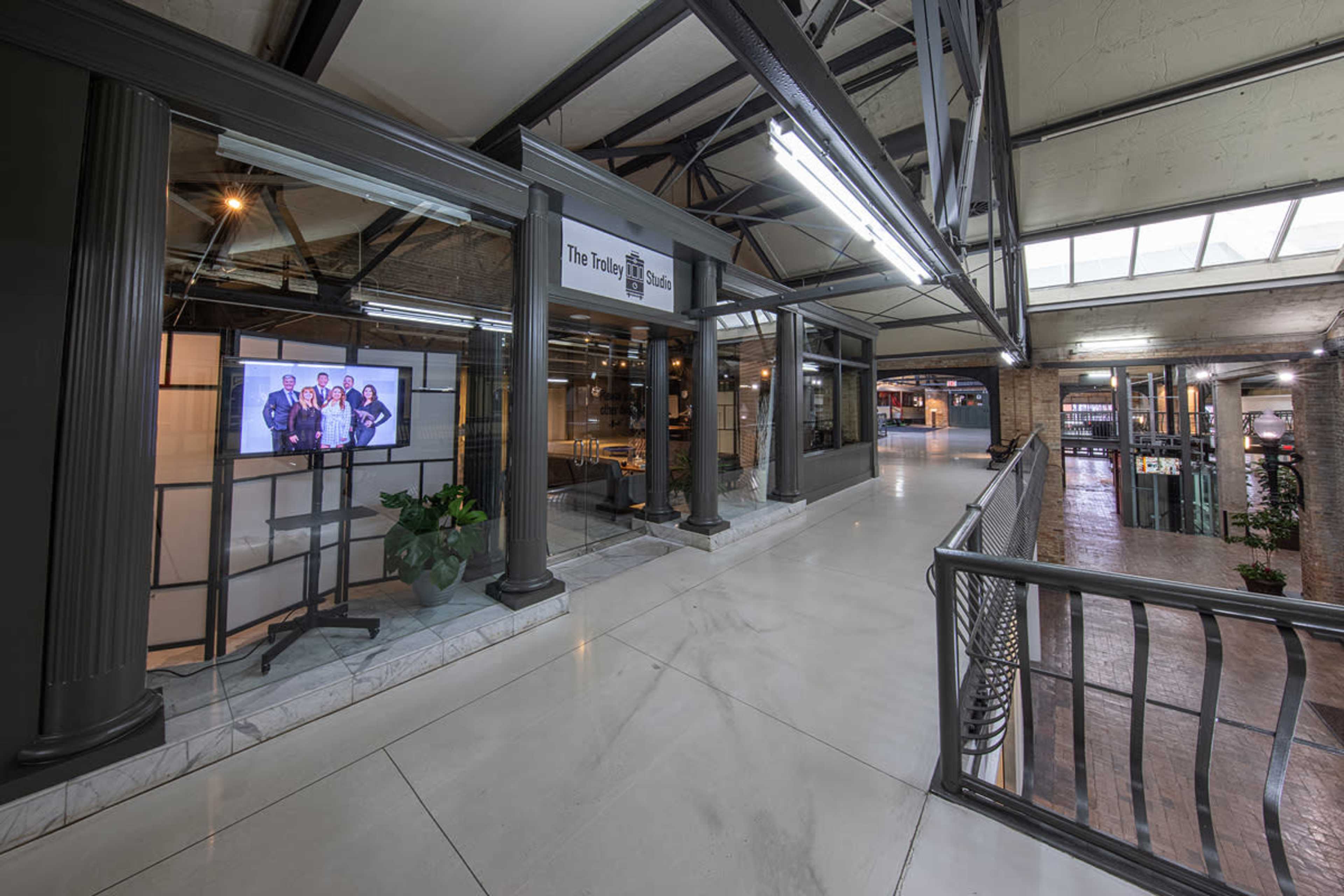 A modern indoor shopping space with open walkways, large windows, and a display screen featuring a group of people.