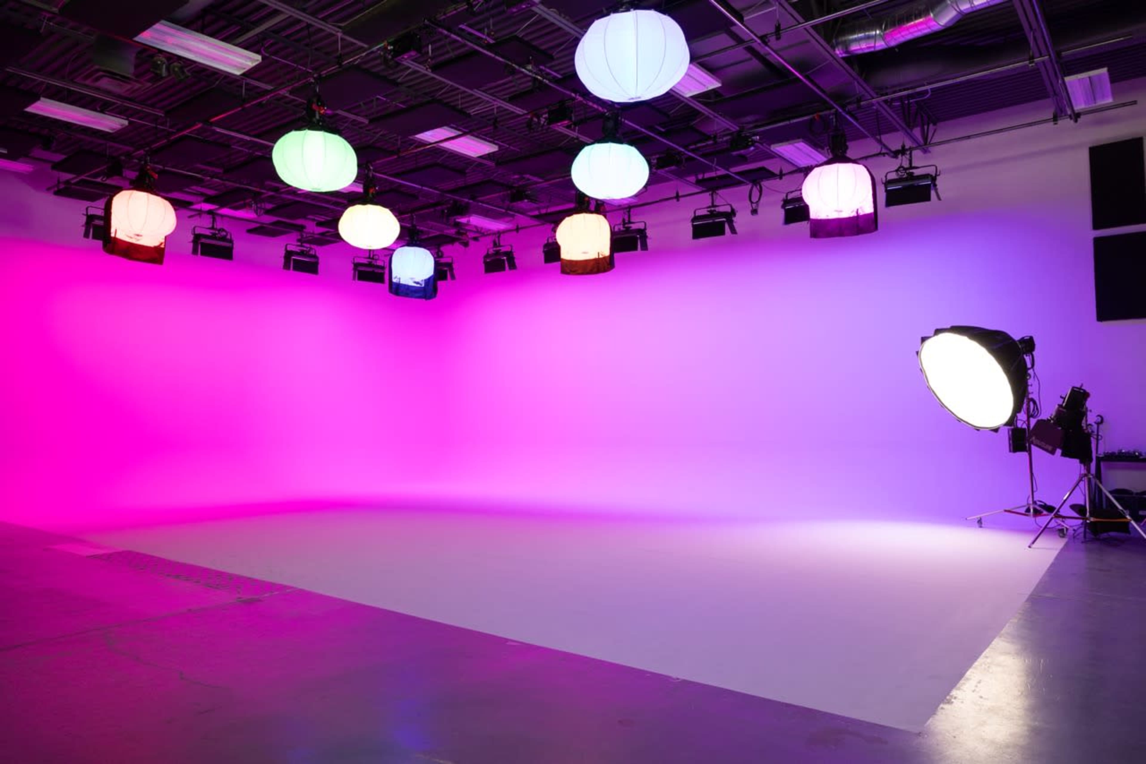 An empty studio space with colorful hanging lanterns and a large light source aimed at a plain backdrop.