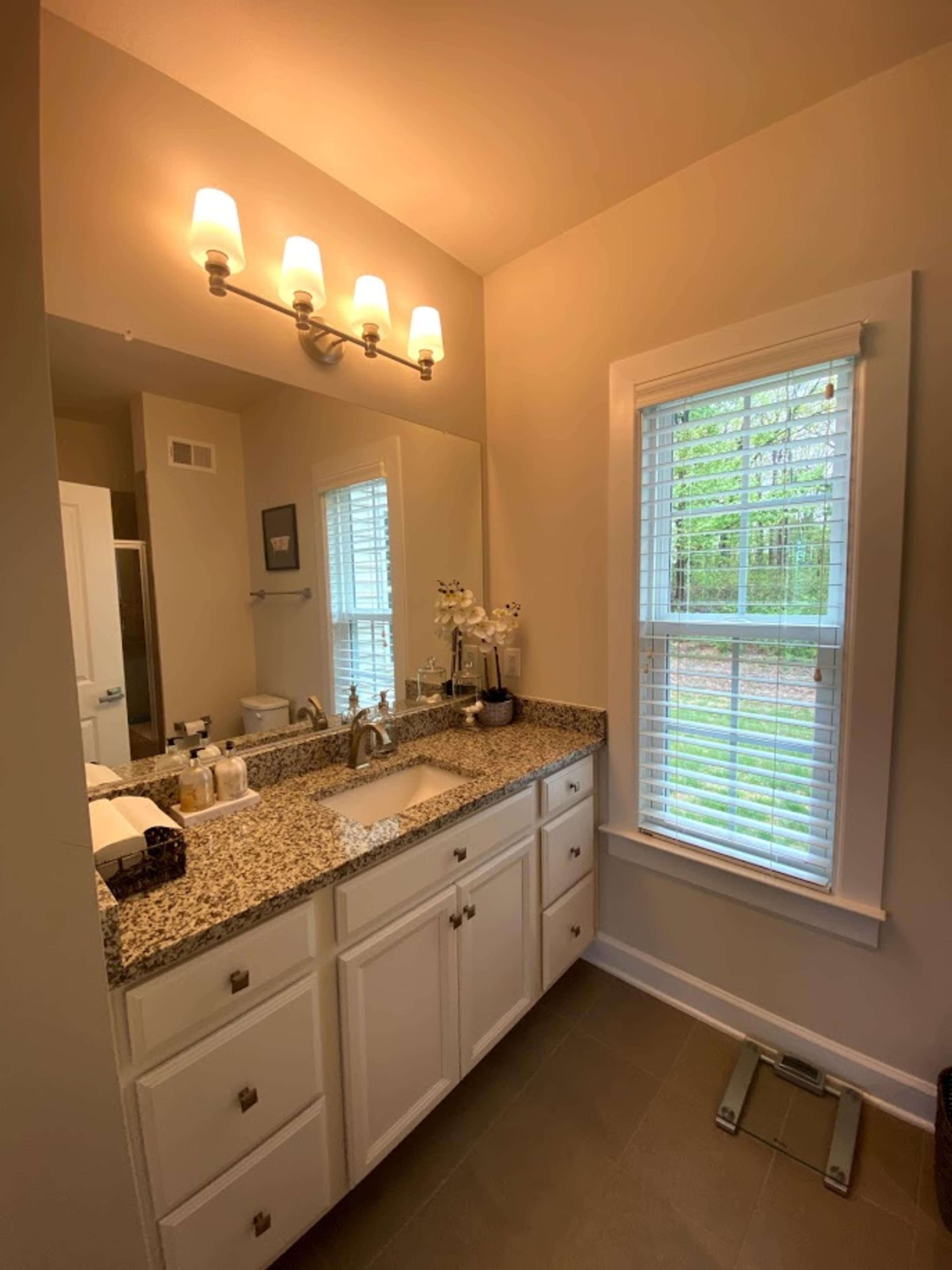 A bathroom with a granite countertop, a sink, a mirror, and a window with blinds.