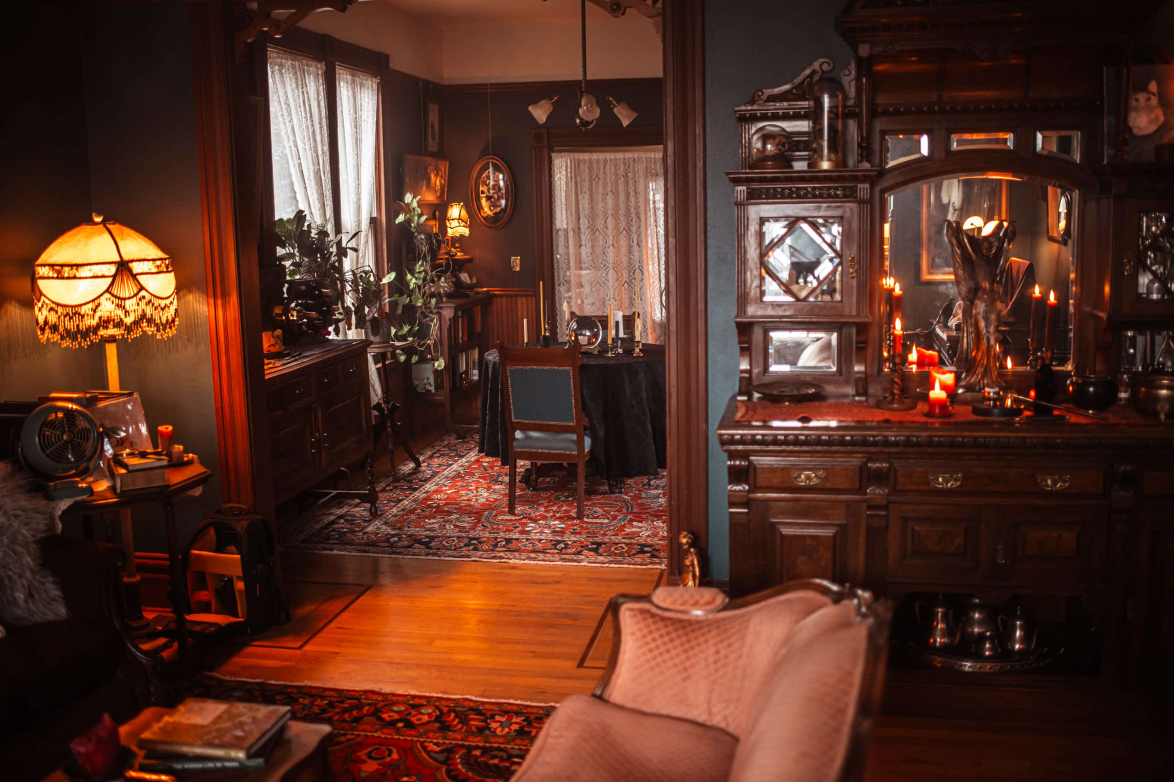 The image depicts a dimly lit vintage living room, featuring an ornate wooden mirror, a table set for dining, and decorative elements like candles and plants.