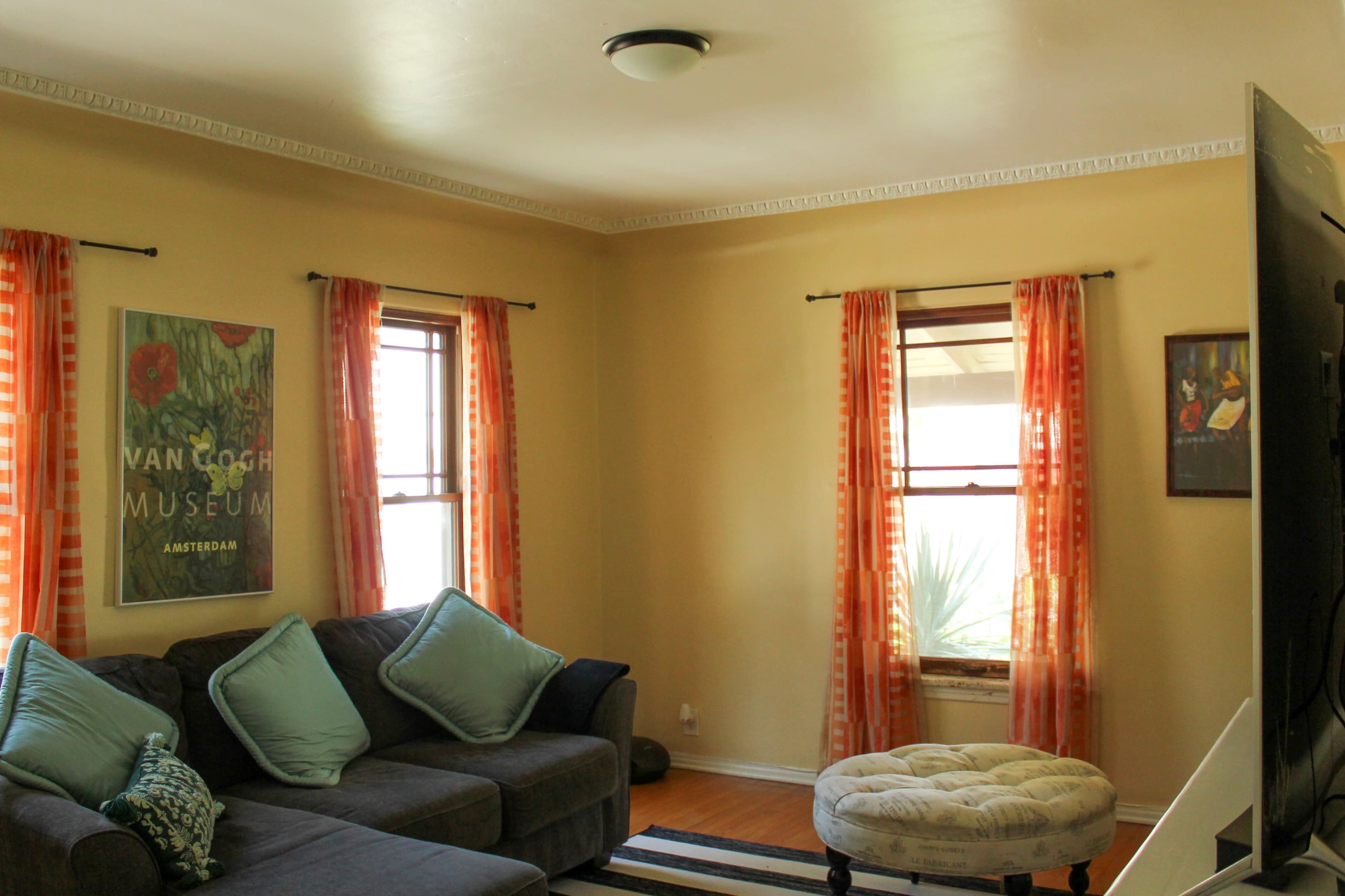 The image shows a cozy living room with a gray sectional sofa, colorful curtains, and artwork on the walls.