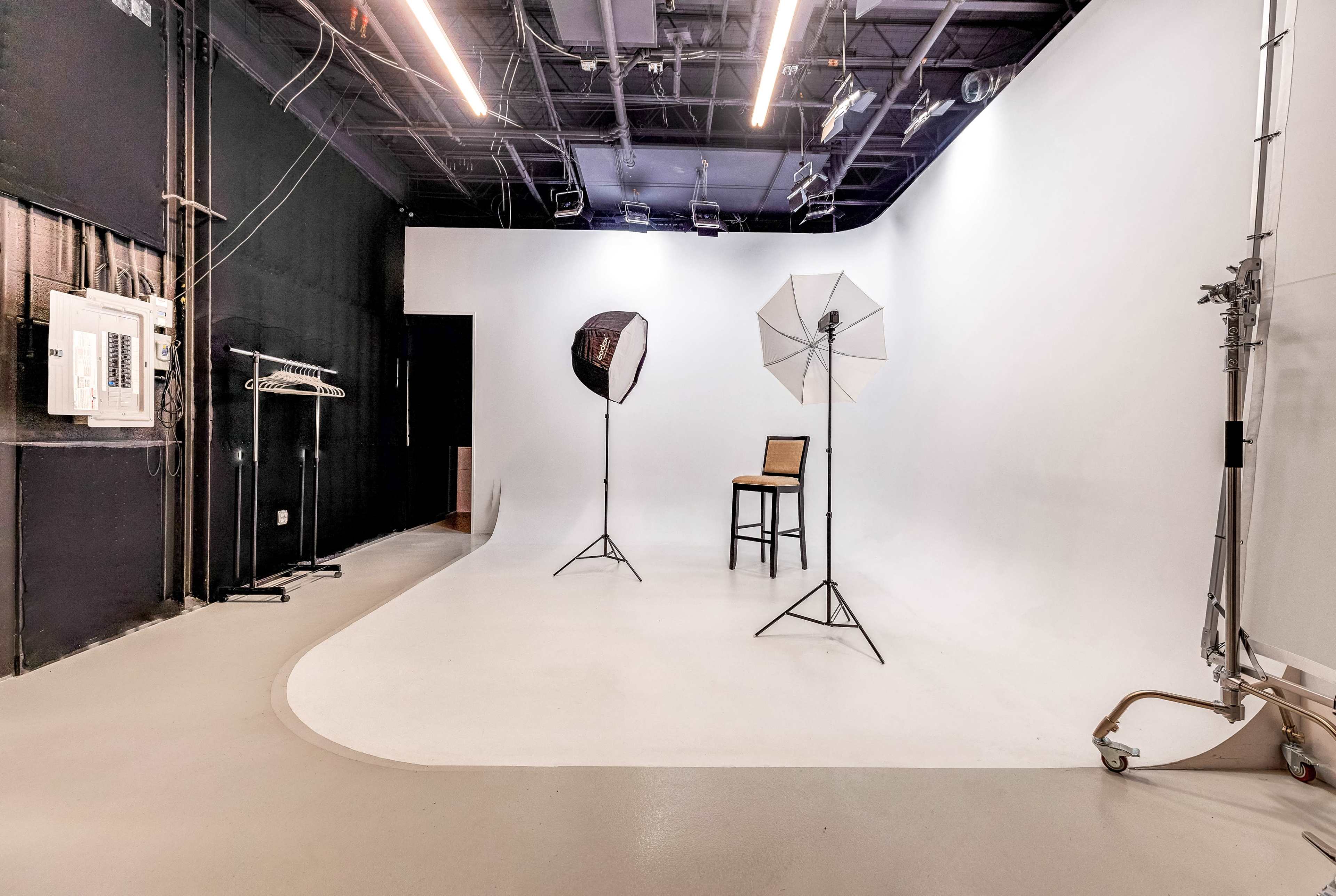 A photography studio with a white curved backdrop, a single chair, and two light stands with softboxes.