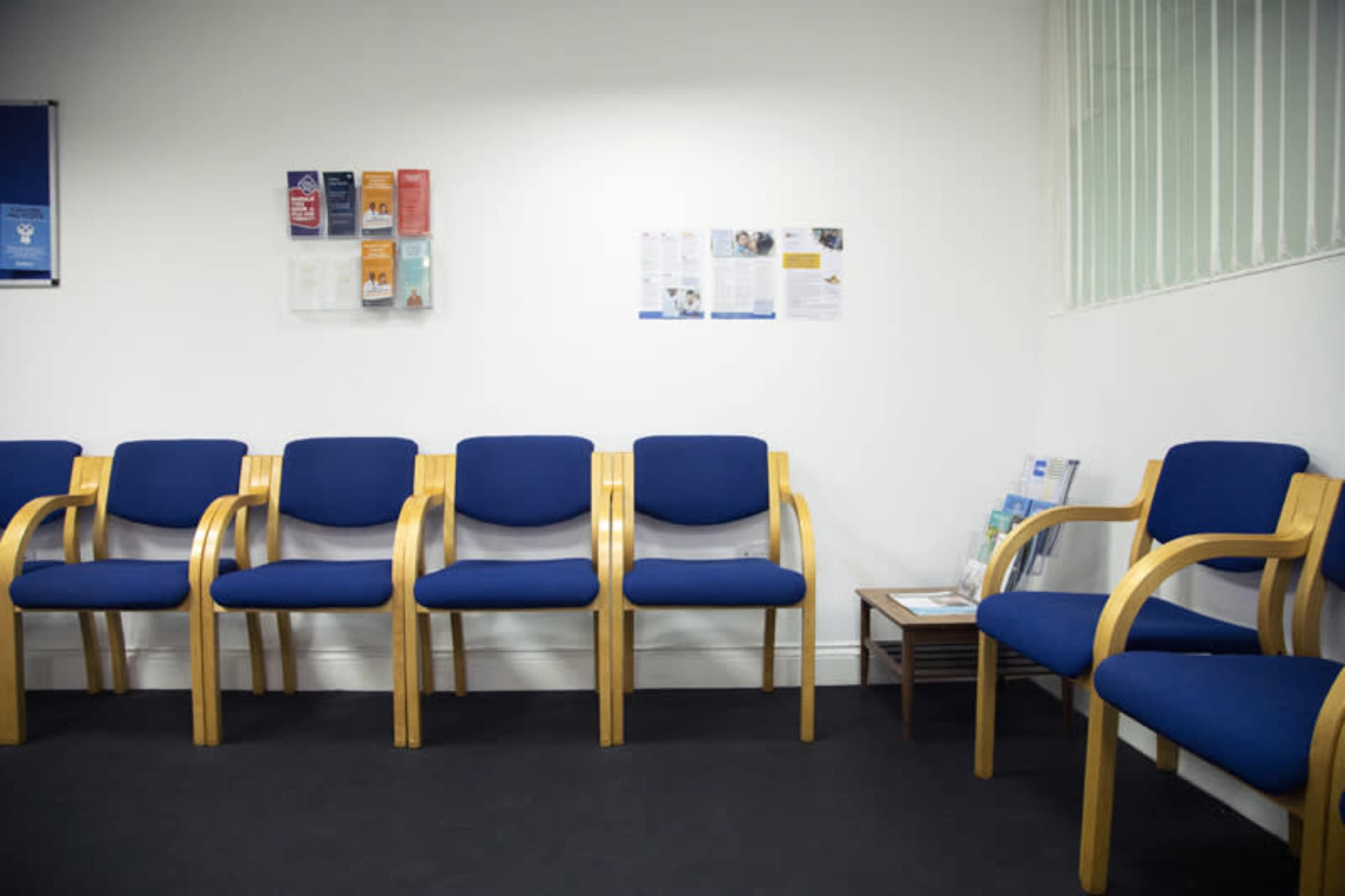 A waiting room with several blue chairs arranged neatly against a white wall, accompanied by informational brochures displayed nearby.