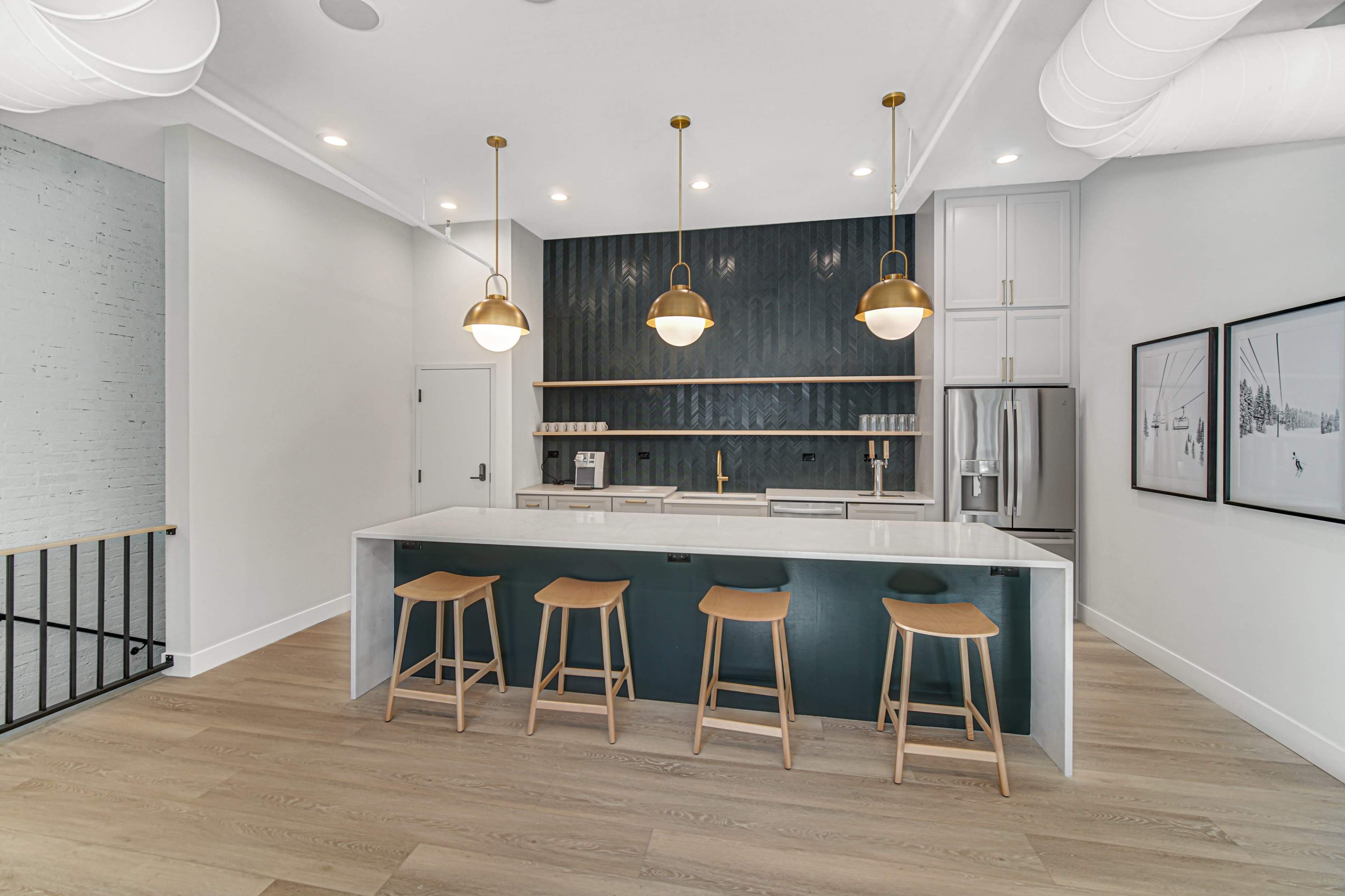 A modern kitchen features a large island with three wooden stools and pendant lighting above, alongside a dark green accent wall and stainless steel appliances.