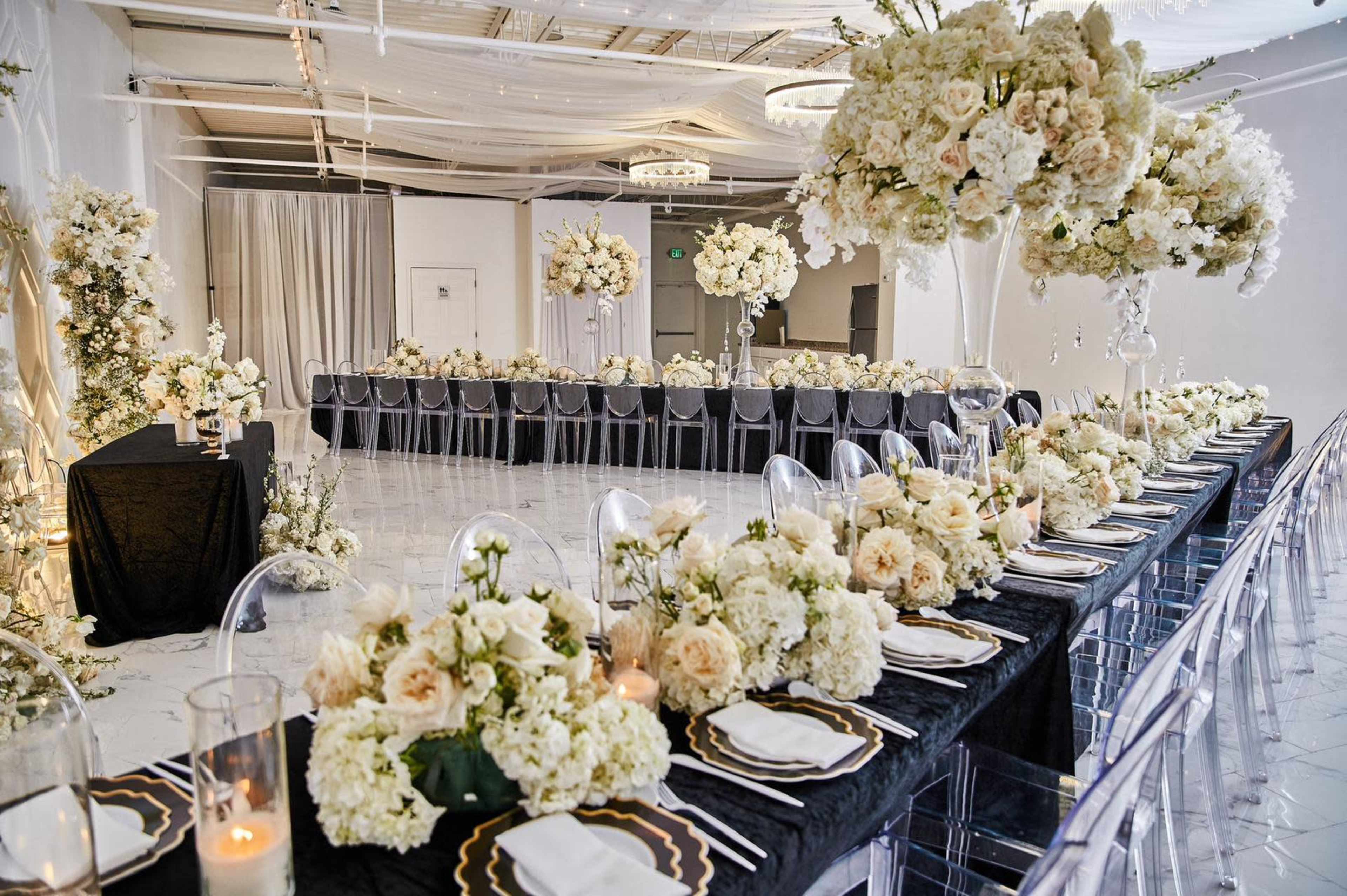 A tastefully arranged banquet hall with multiple tables set for an event, adorned with floral centerpieces and elegant black and white table settings.