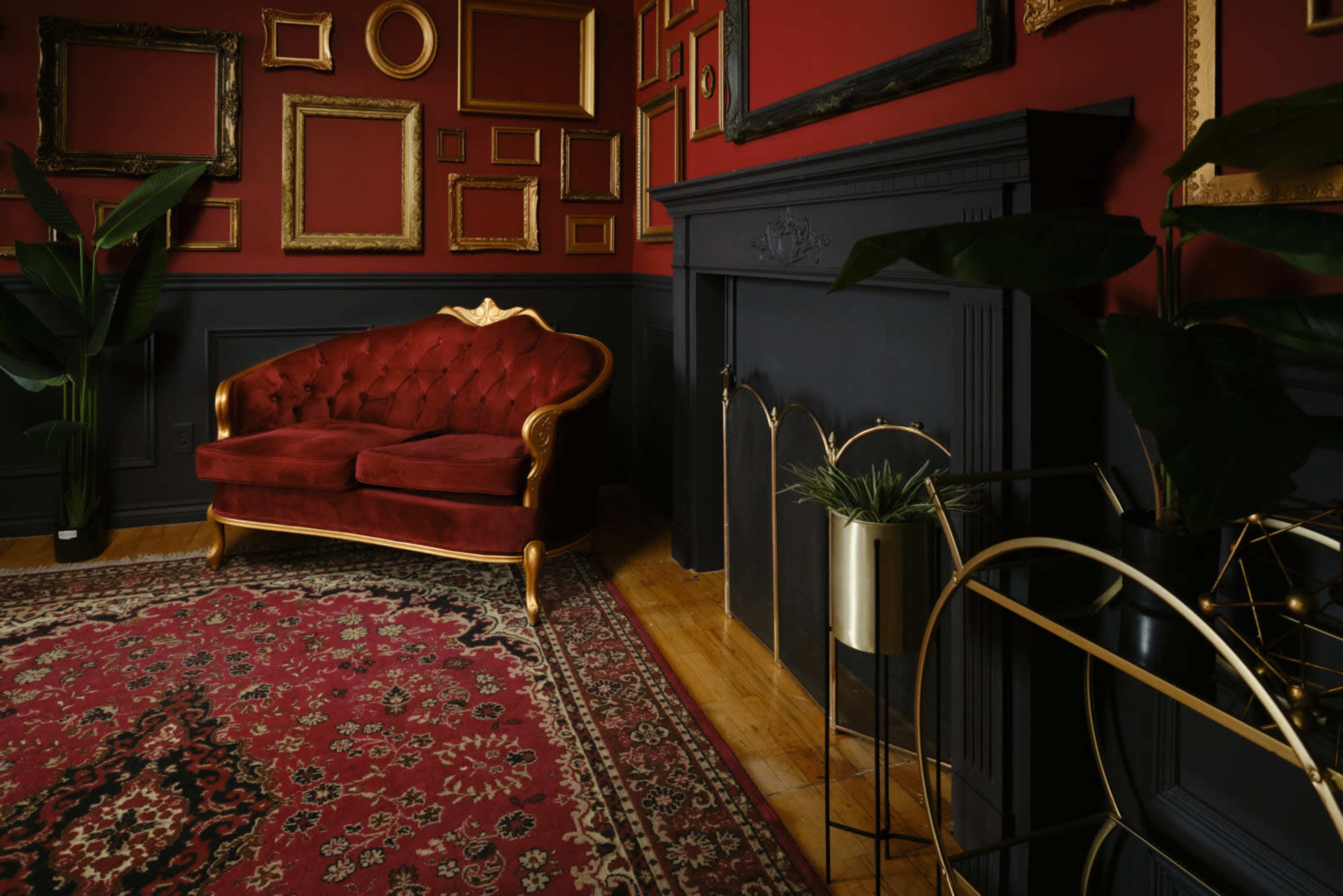The image features a richly decorated interior with a red wall, a vintage velvet sofa, an ornate fireplace, and various empty picture frames.